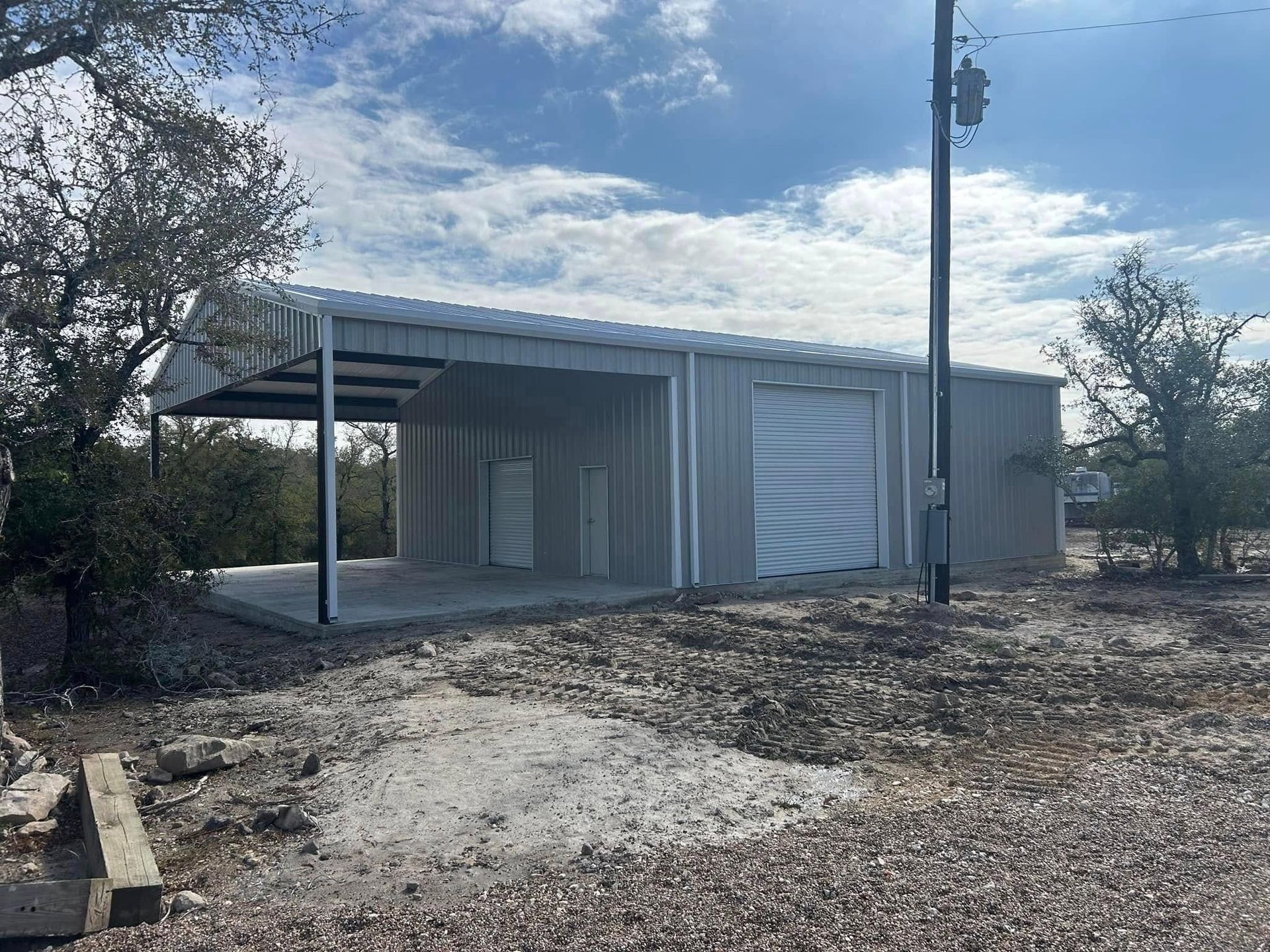 Small metal shed with carport in a dry, rural lot under a partly cloudy sky