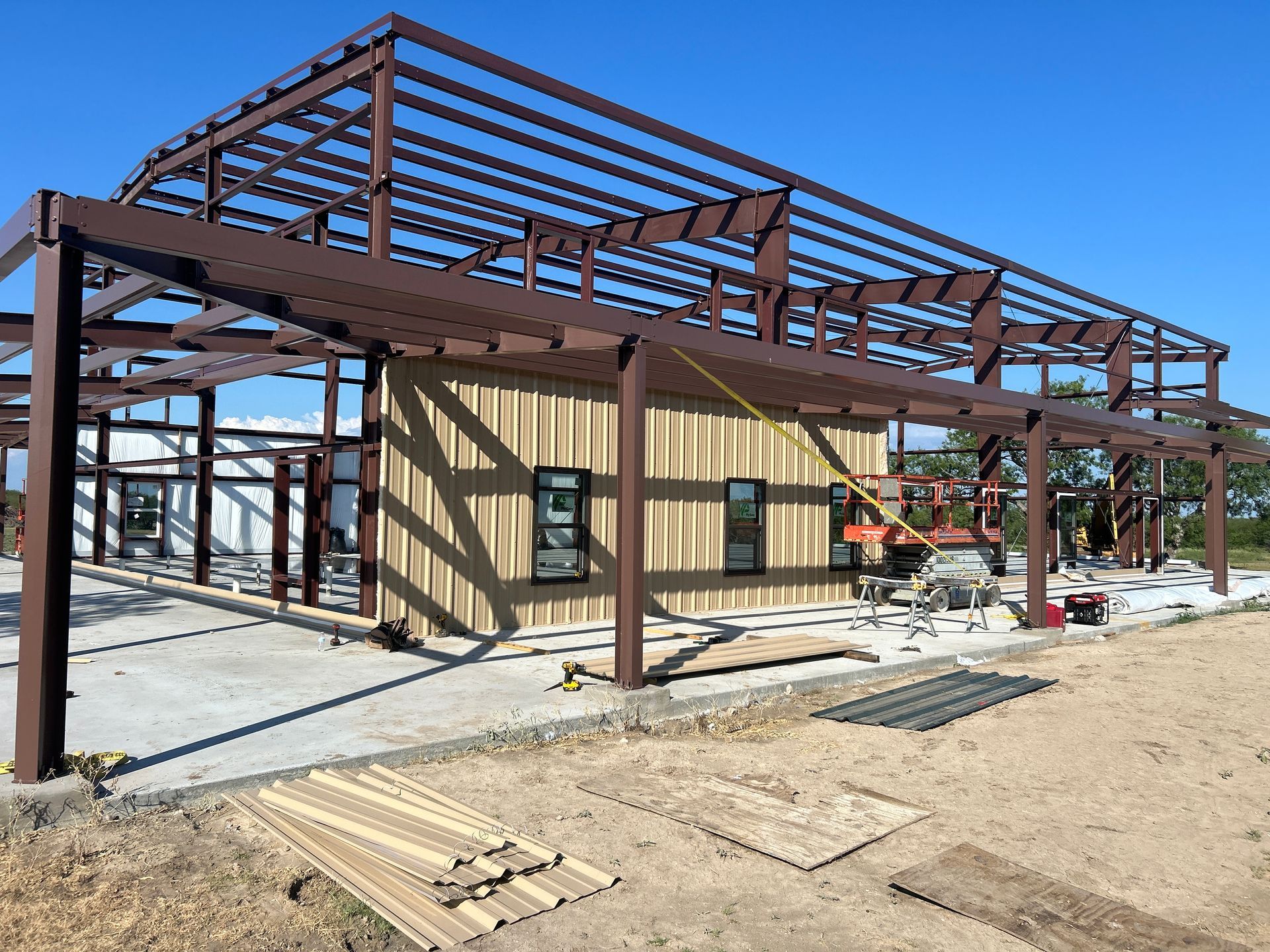 Steel building under construction with tan siding and dark metal frame on a concrete slab