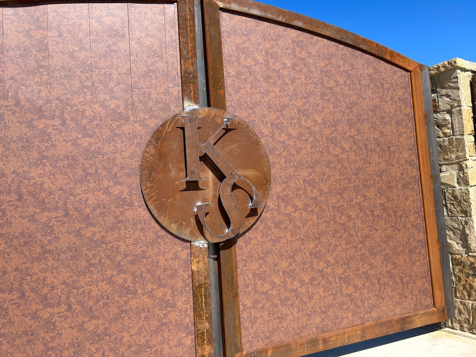 Rusty metal gate with a circular emblem mounted on a stone post