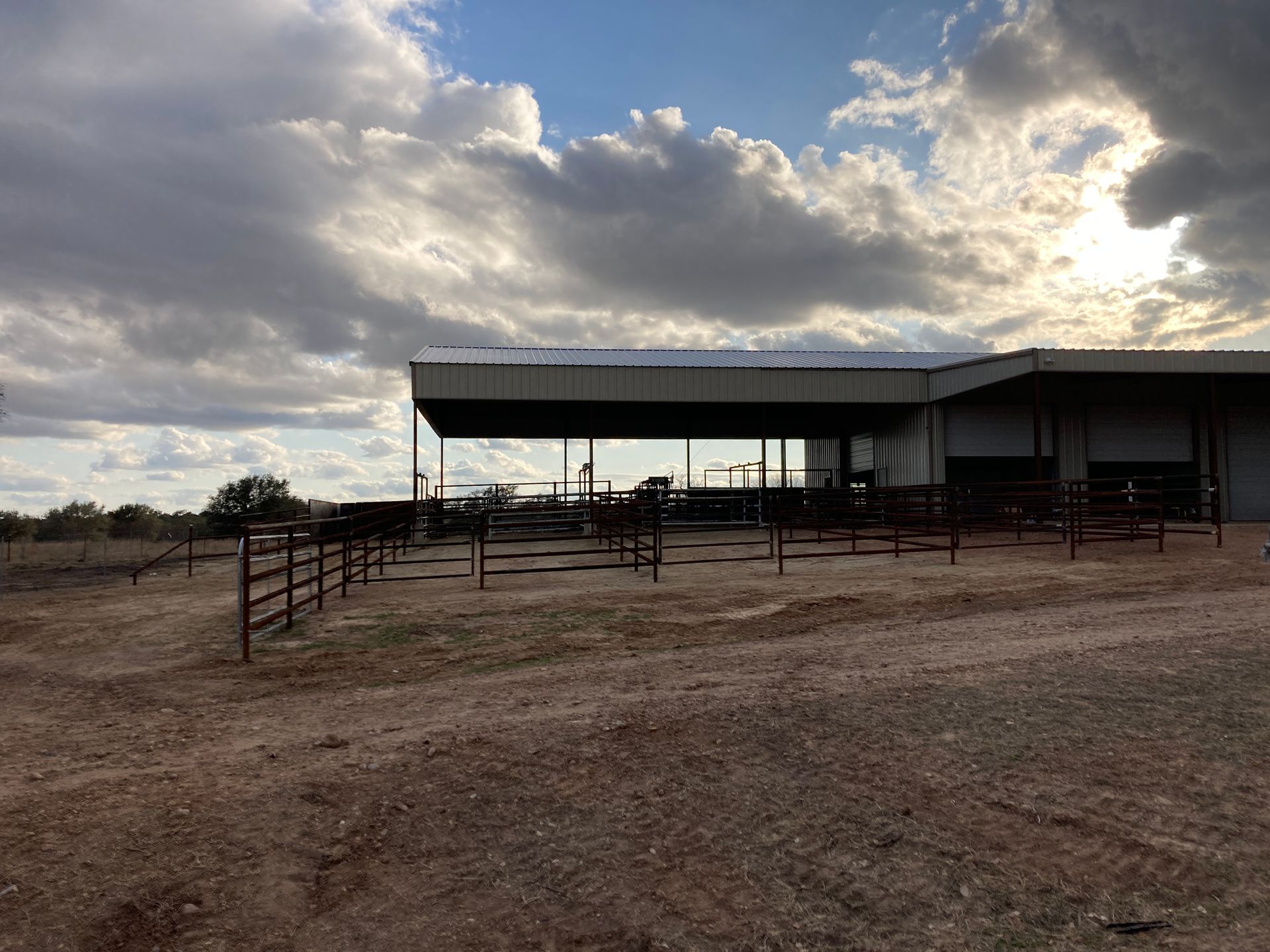 Rural livestock pen with metal shelter under a cloudy sky on a dirt lot