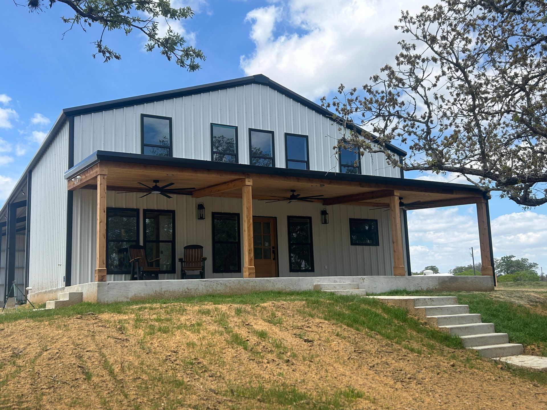 Large gray metal warehouse with a covered entry and white propane tank under a cloudy blue sky