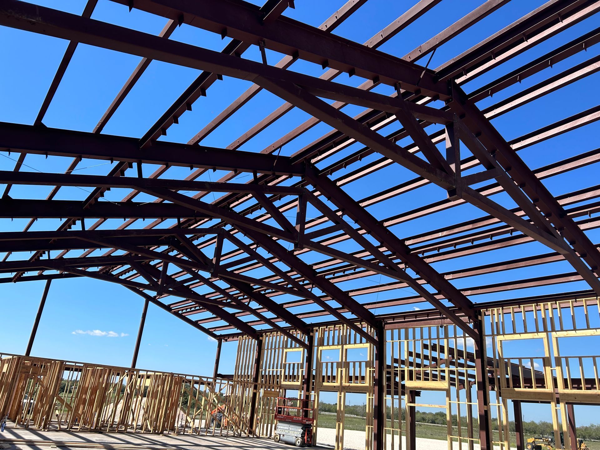 Construction site with workers pouring a concrete slab beside a metal building under a blue sky