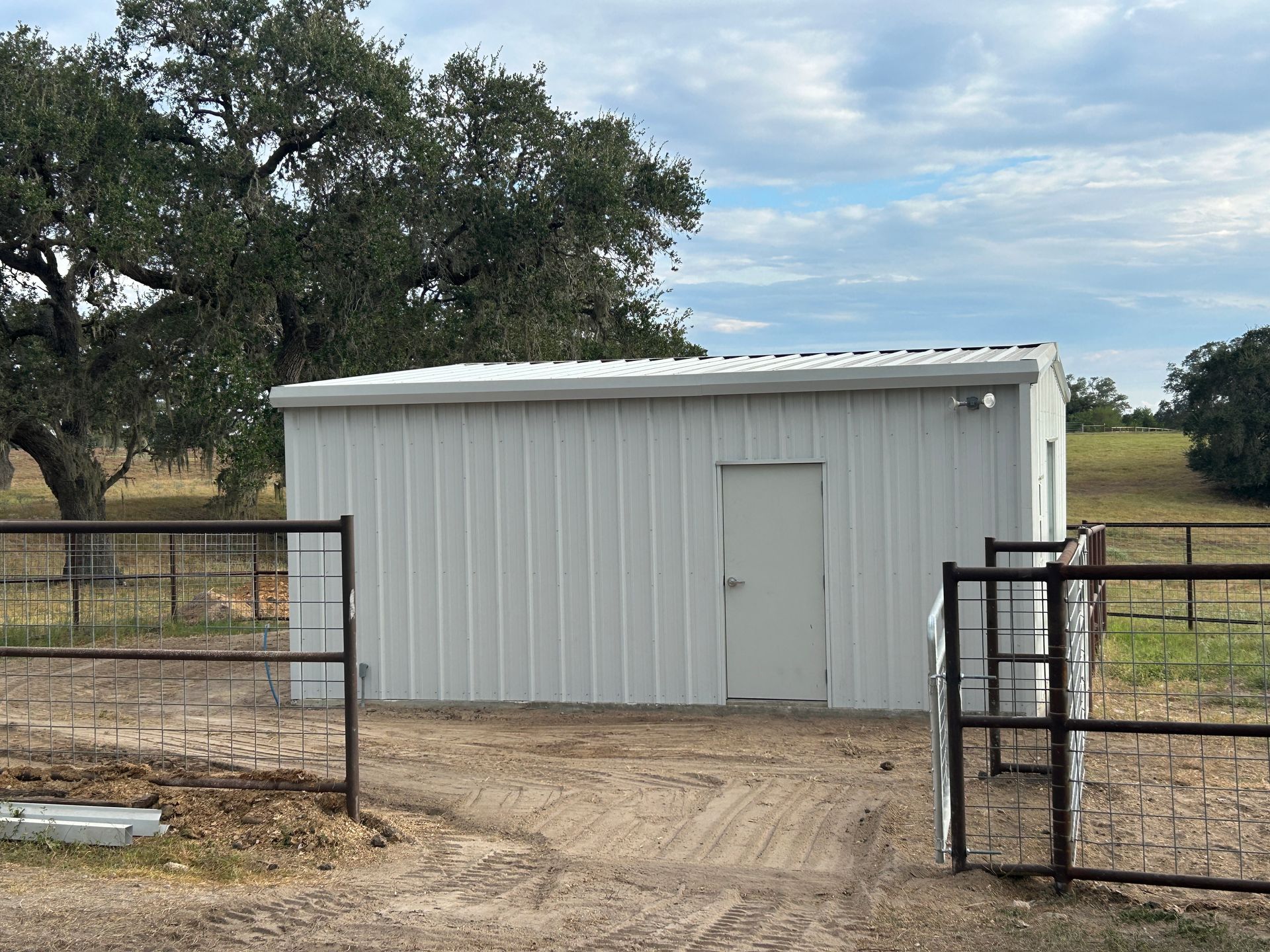 White metal storage shed with a roll-up door on a dirt lot under a cloudy sky