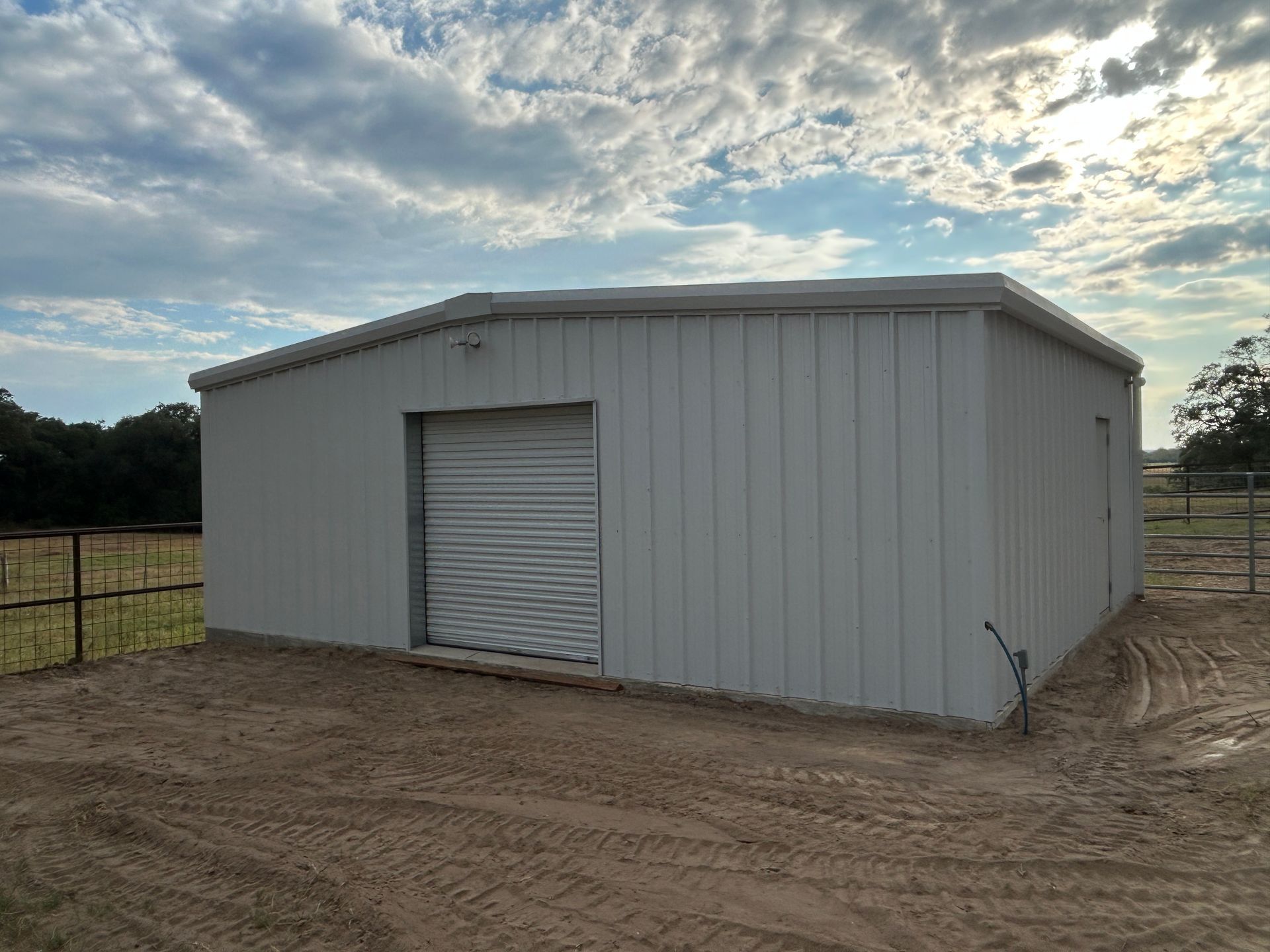 White metal barn with a roll-up door on a dirt lot under a cloudy sky
