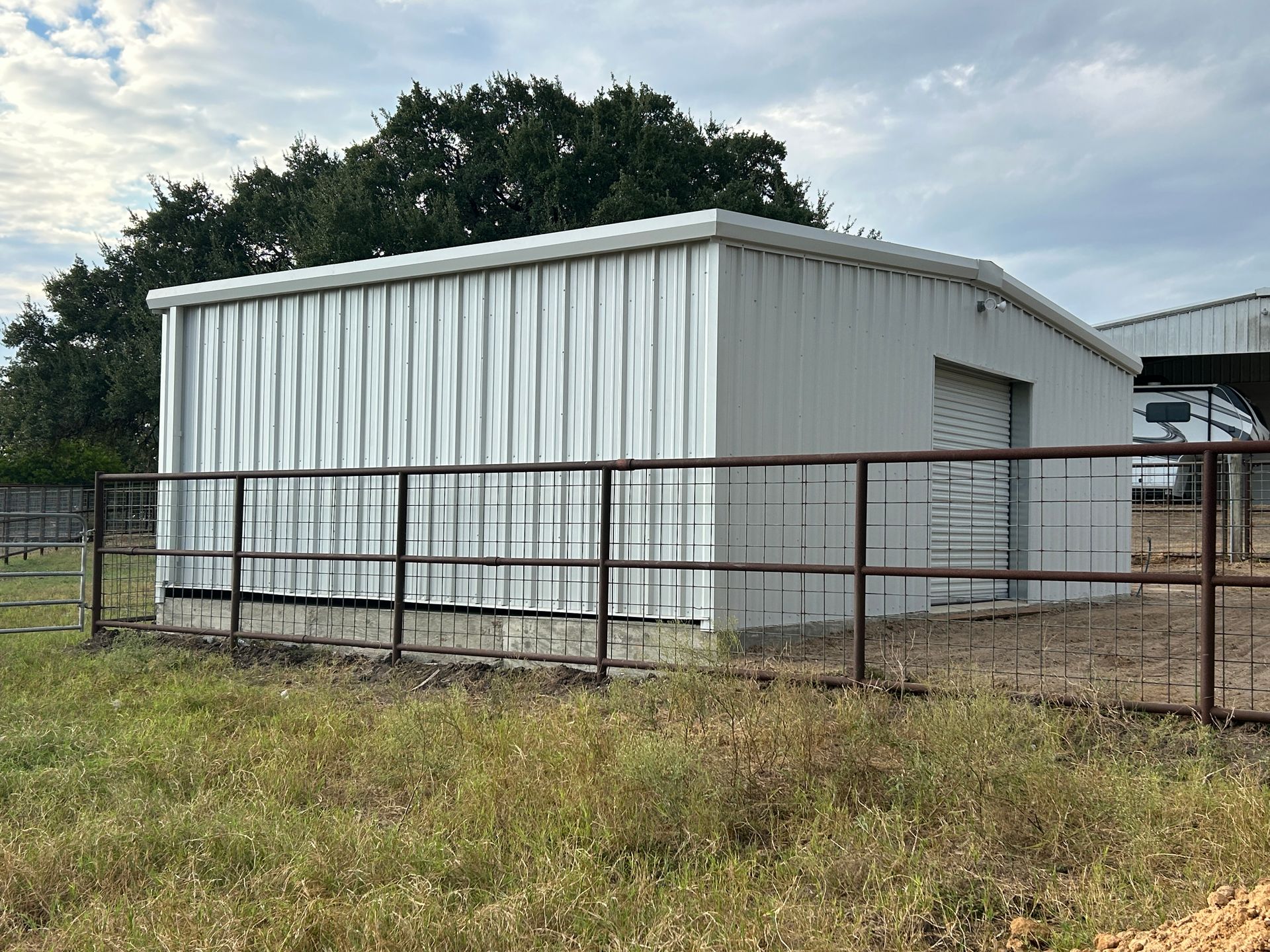 White metal shed in a fenced rural field under a cloudy sky