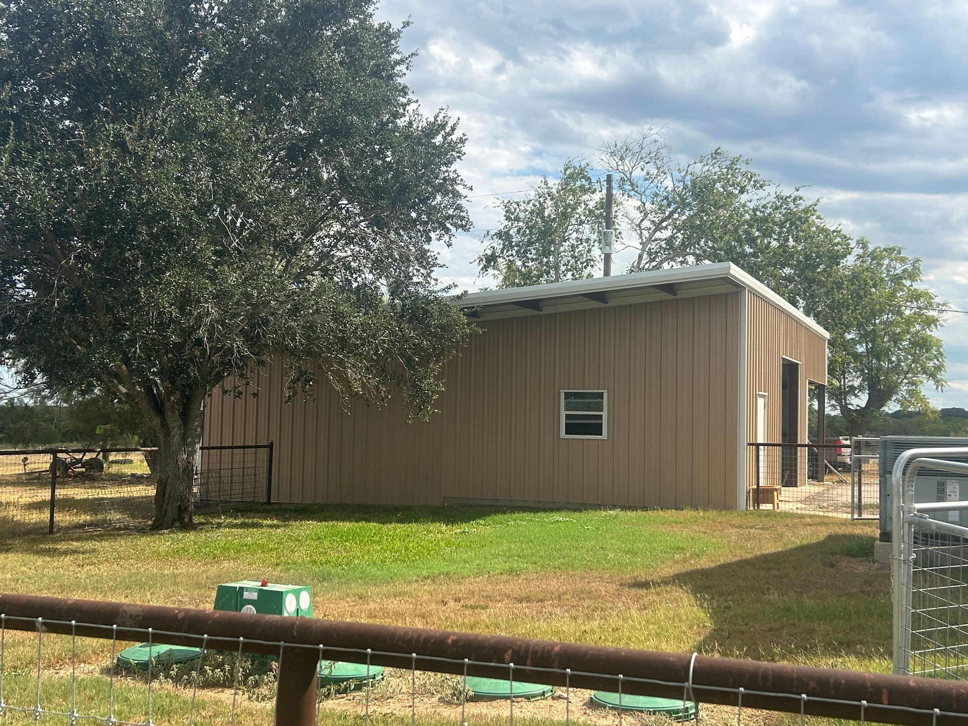 Small open-sided shed with a metal roof in a grassy yard under a cloudy sky.