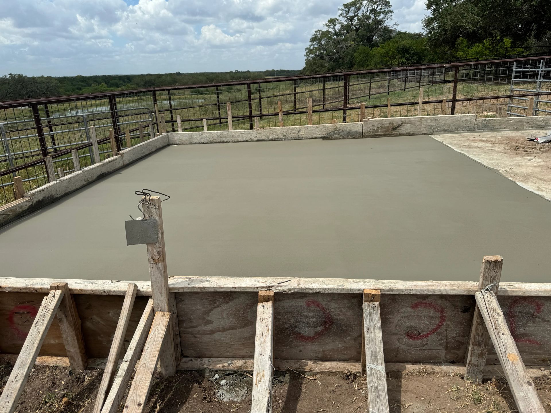 Freshly poured concrete slab with wooden formwork in a rural outdoor setting under cloudy sky