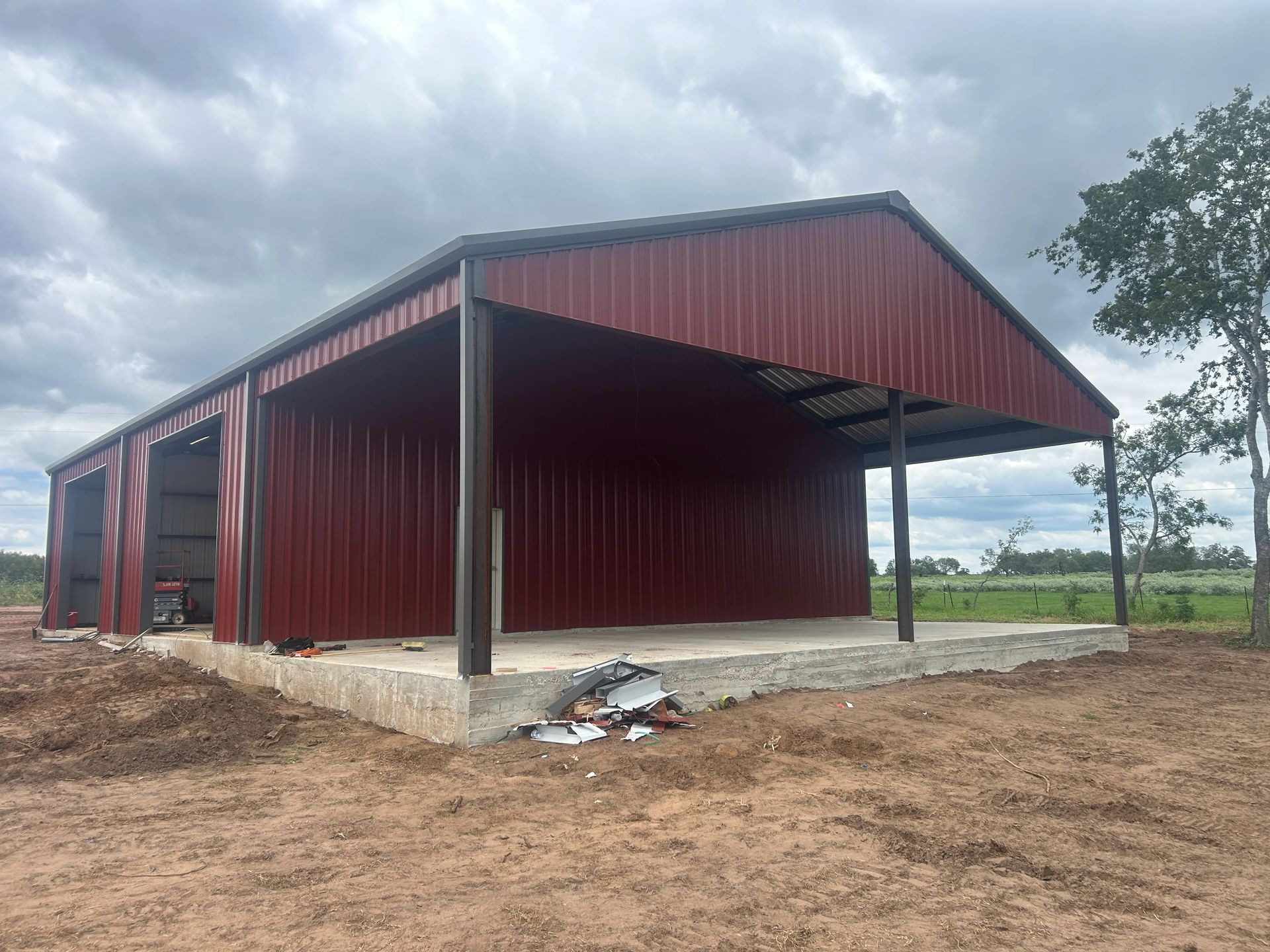 Red metal barn-style shed with open front, on a concrete pad in a muddy rural field under cloudy skies