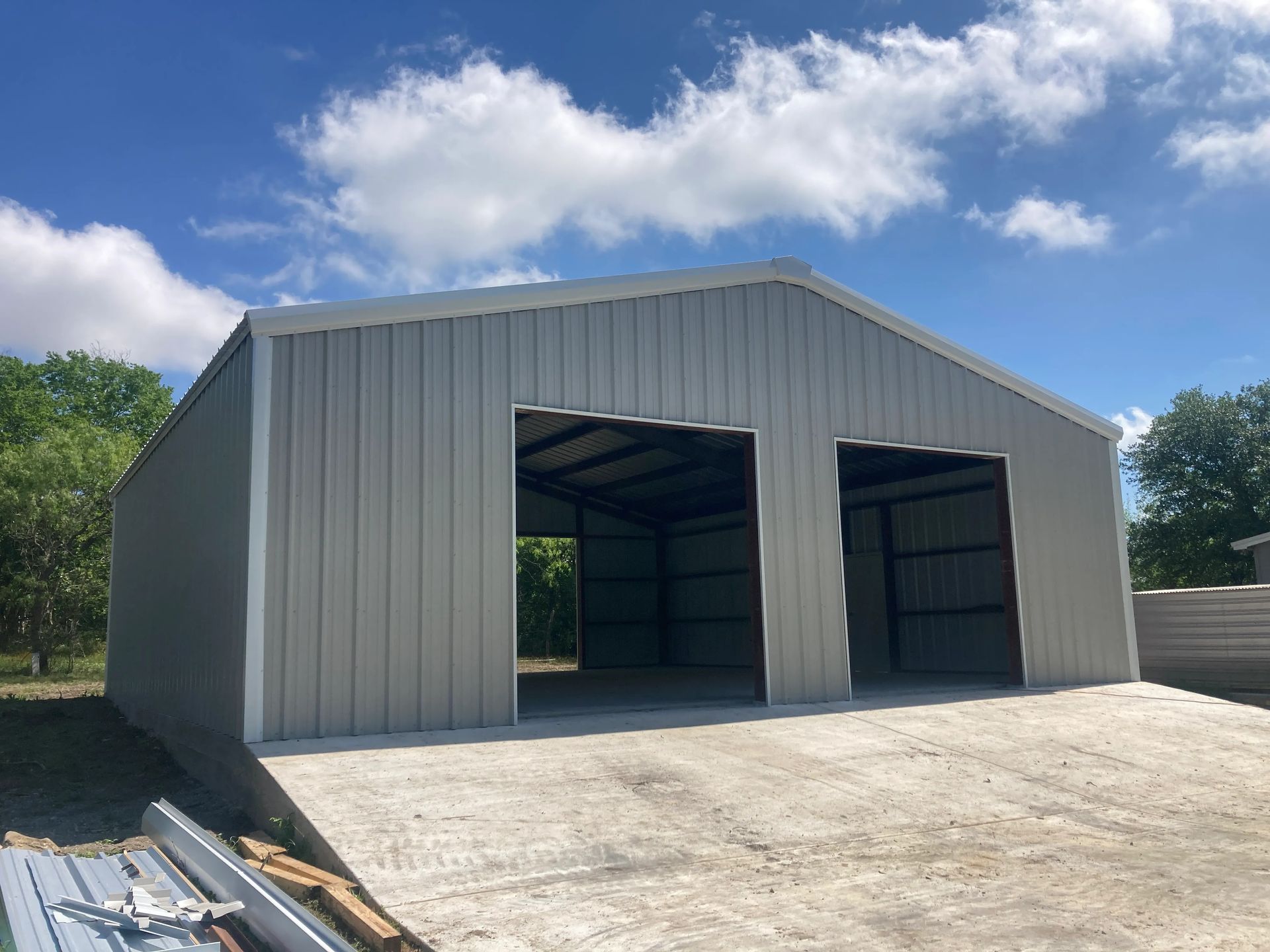 Large gray metal warehouse with two open bays and a sloped concrete apron under a blue sky
