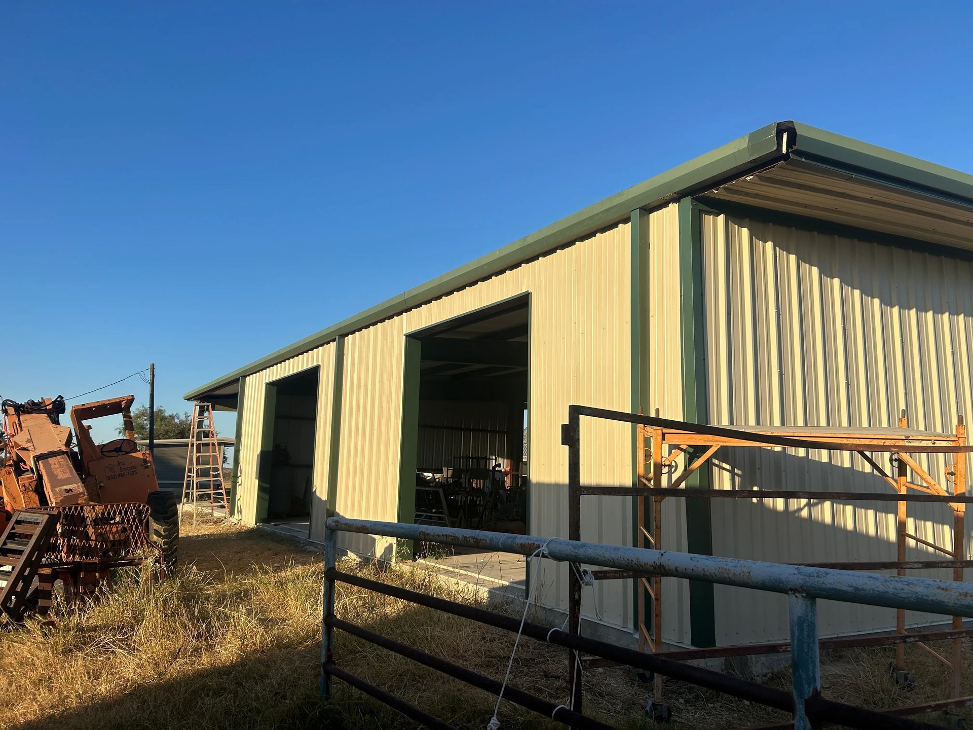 Metal barn with open doors and a fenced pen on a dry farm under a clear blue sky