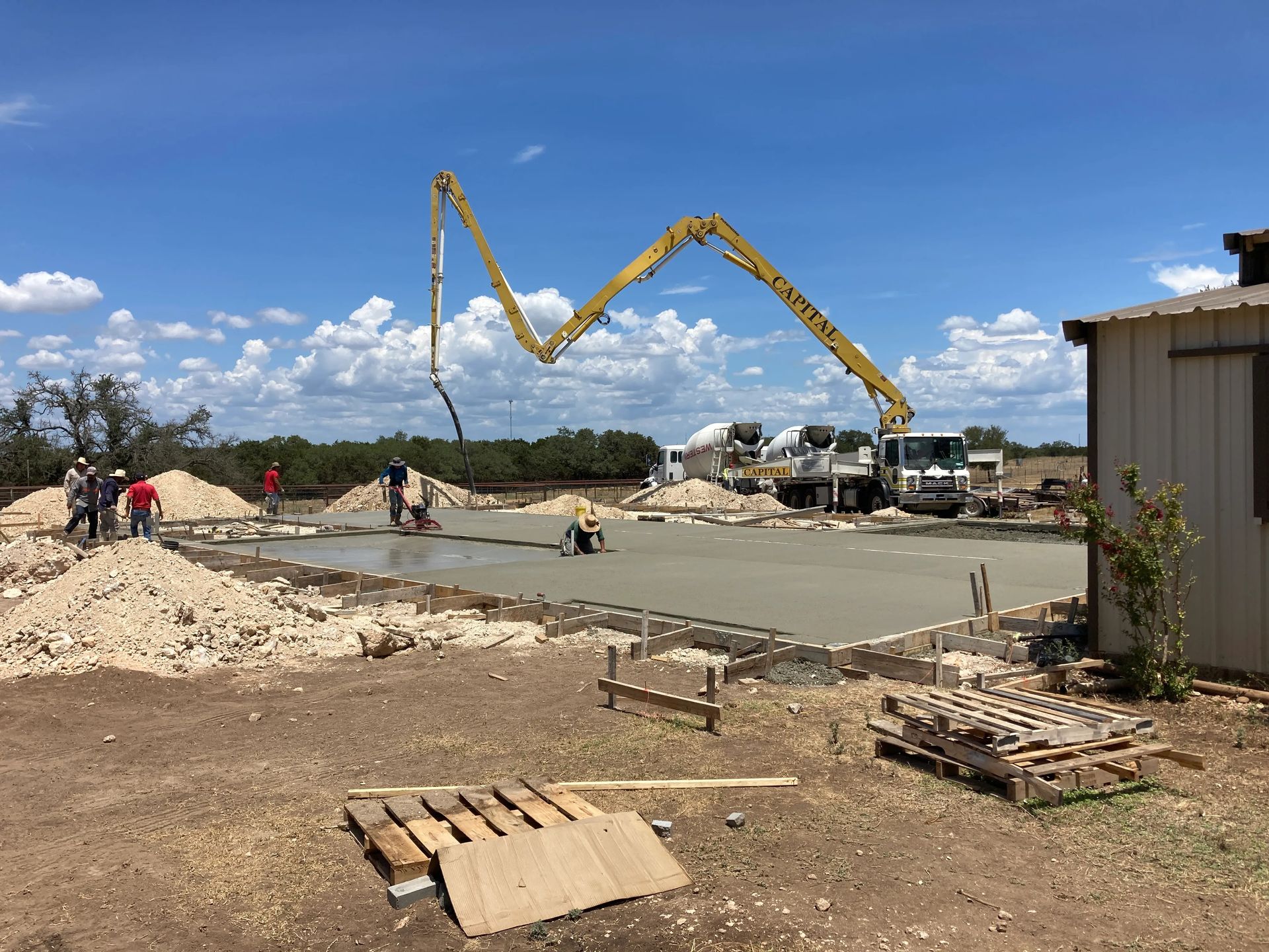 Construction site with concrete being poured by a boom pump and workers around a slab foundation