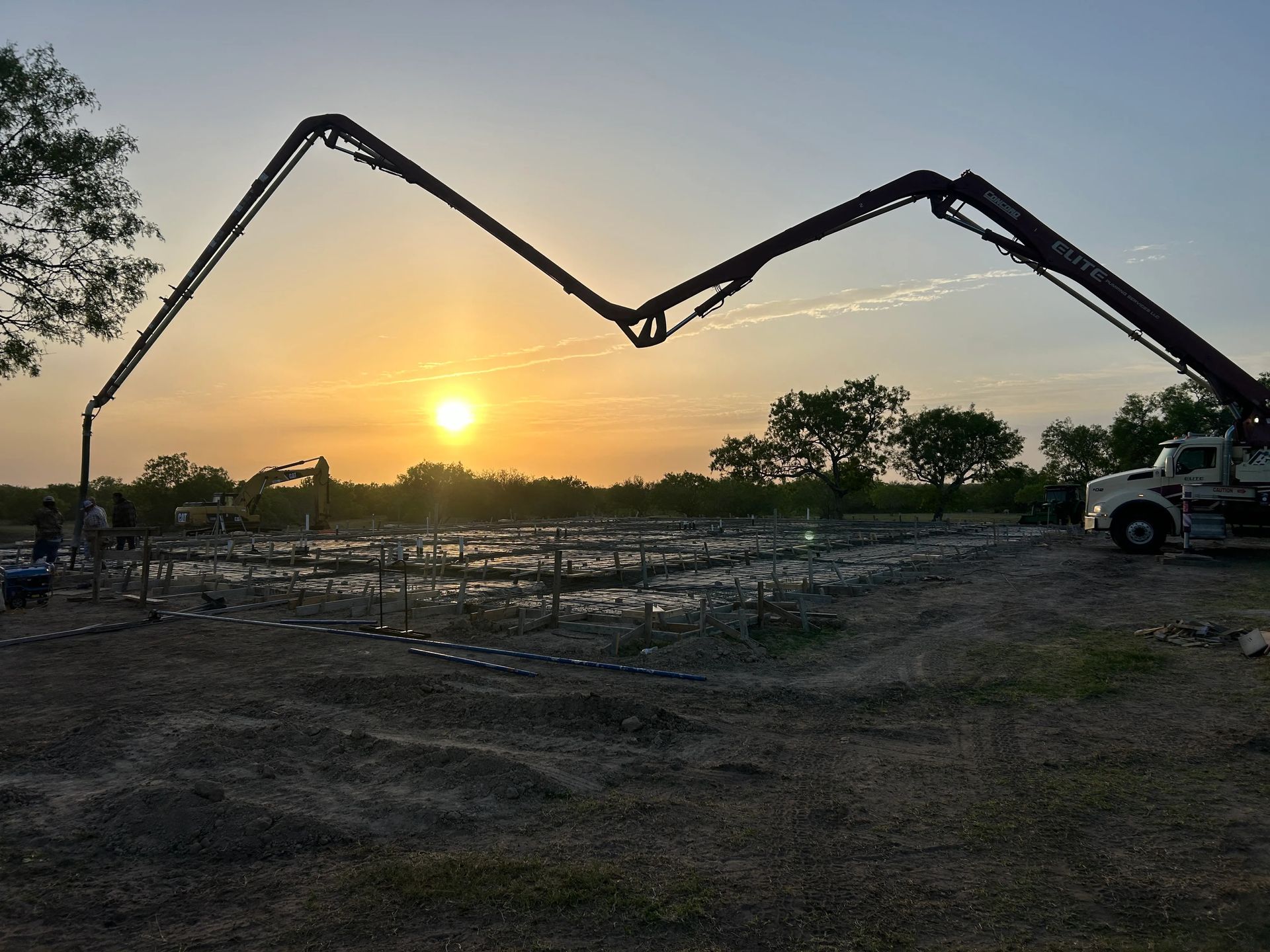 Concrete pump truck pouring at sunset over a muddy construction site.