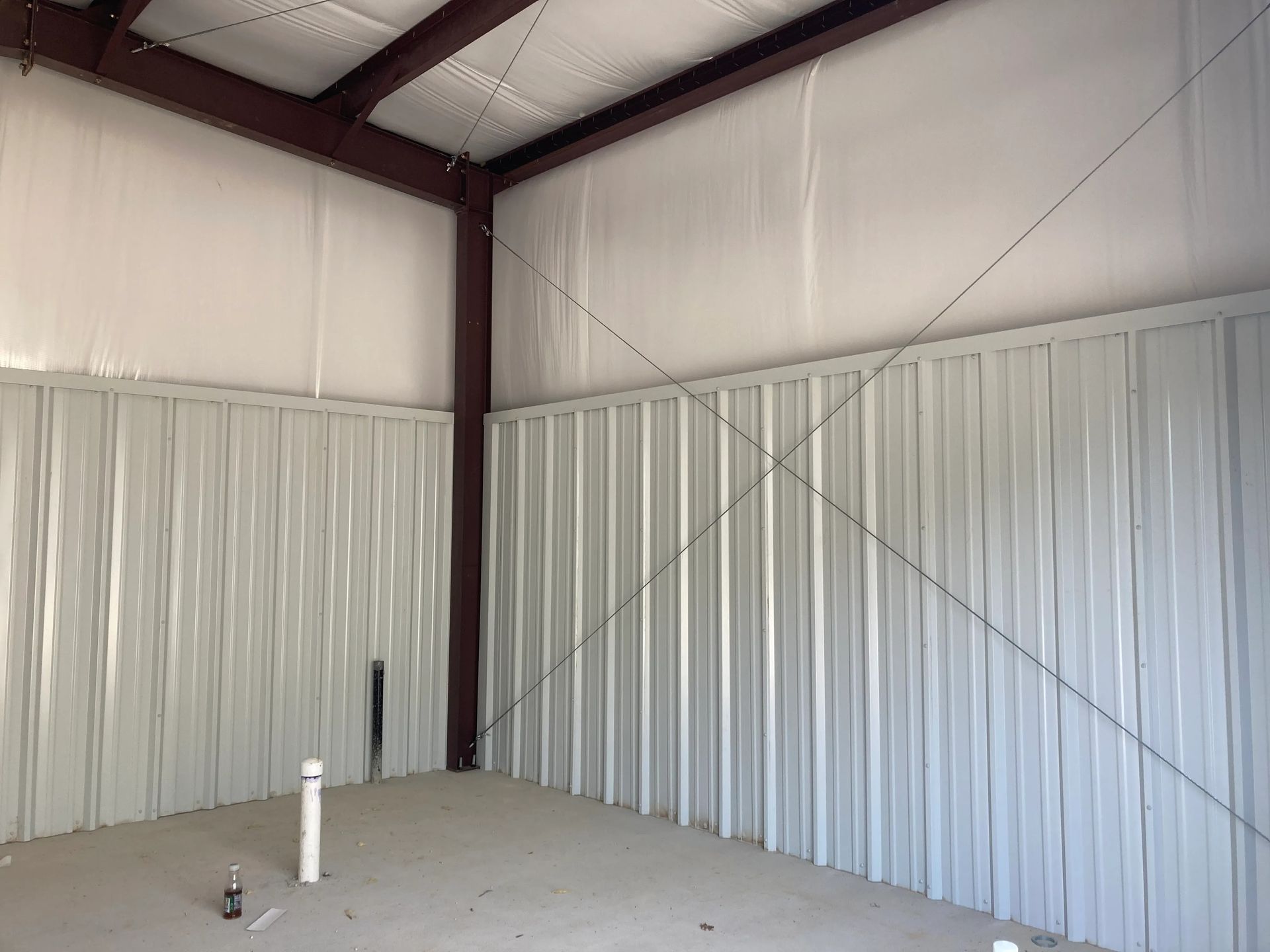 Empty metal warehouse interior with corrugated walls, white lower panels, and exposed steel beams.