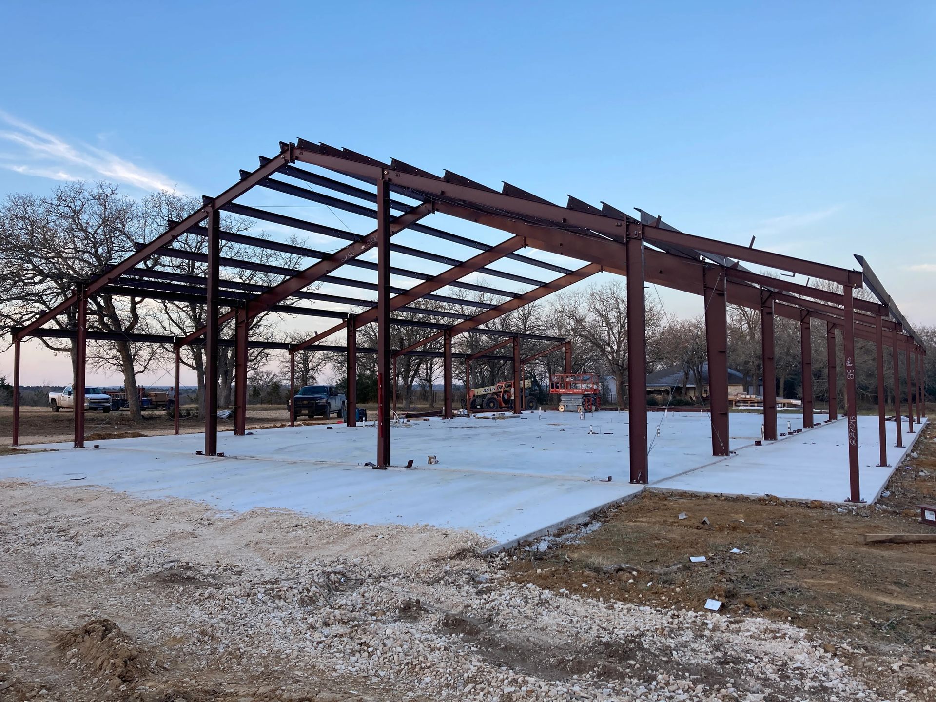 Steel building frame under construction on a snowy lot under a clear blue sky