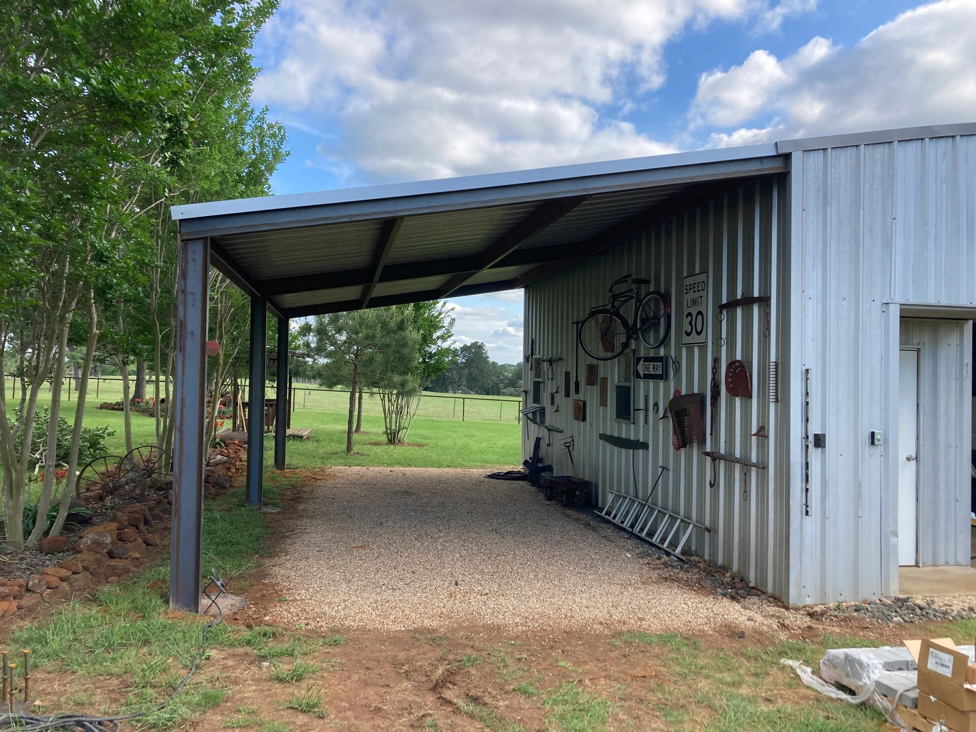 Small metal shed with a covered gravel parking area beside grassy trees, covered in graffiti.