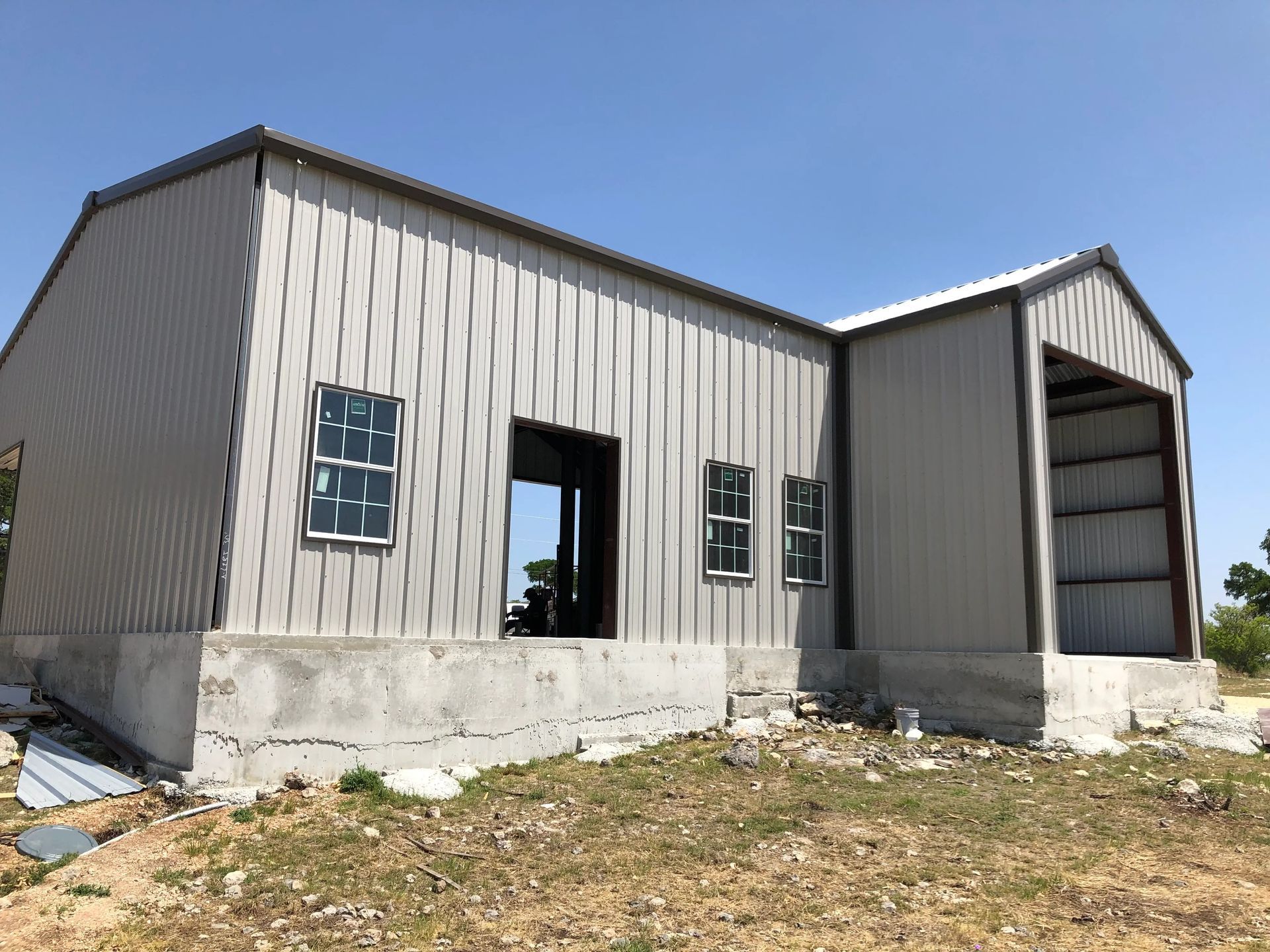 Abandoned gray metal building with broken windows and a large open doorway under a blue sky