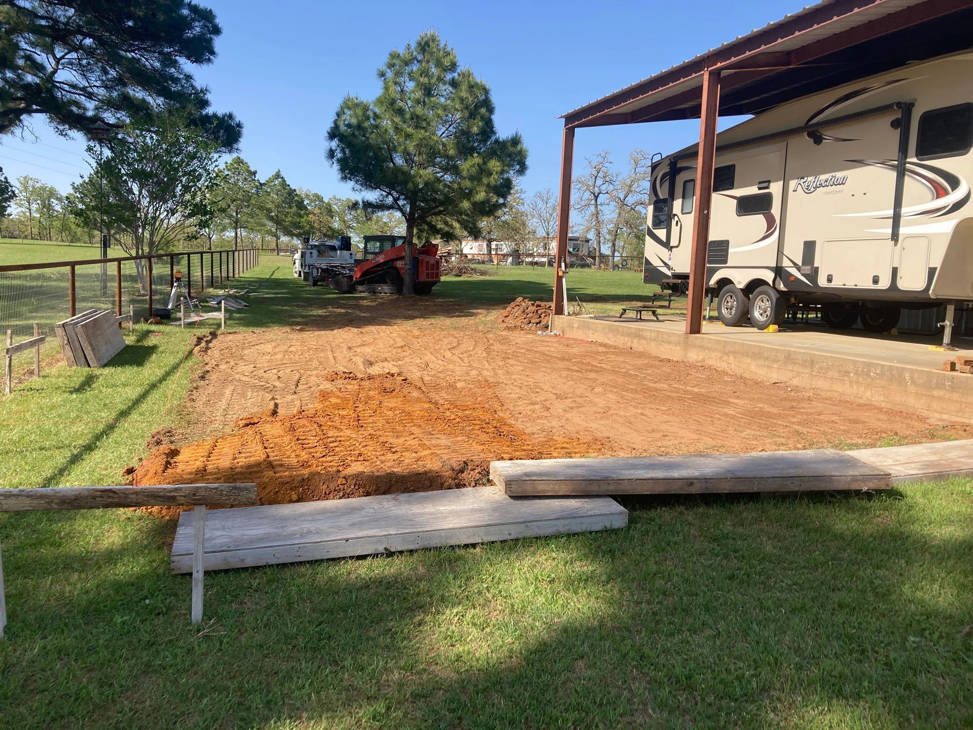 Gravel driveway under construction beside a covered RV and red truck in a rural yard.