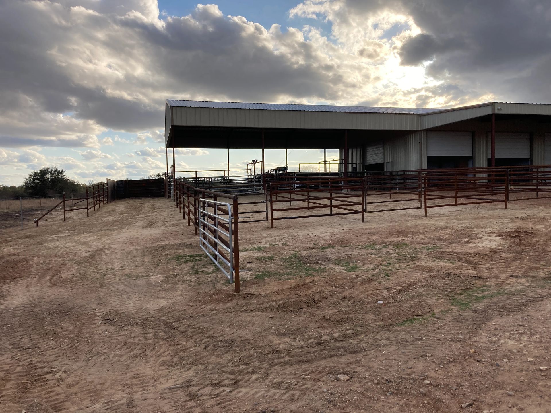 Rural livestock corral beside a metal shed under a cloudy sky at sunset
