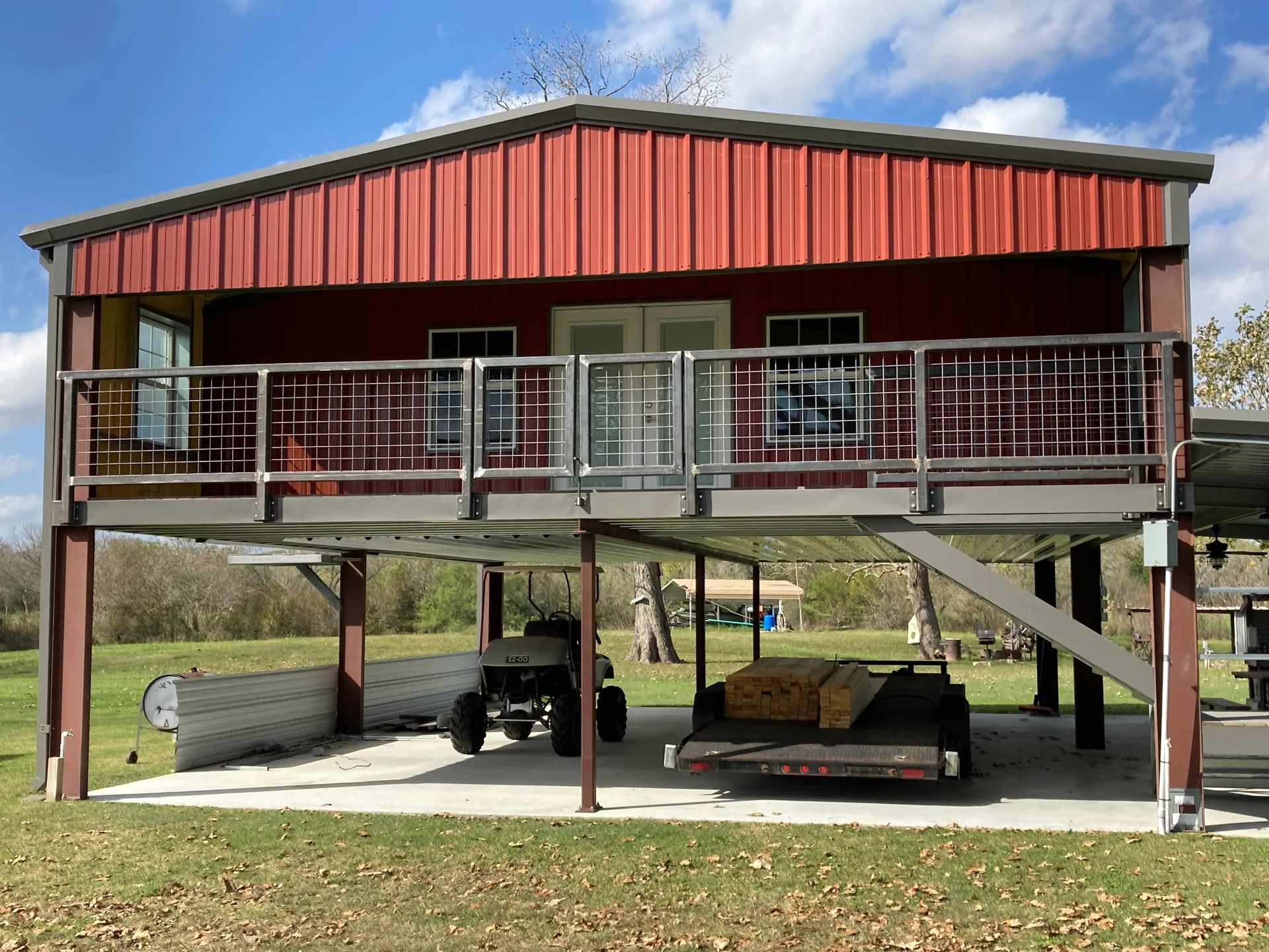 Red elevated house with red roof, front porch, and carport underneath on a hillside.