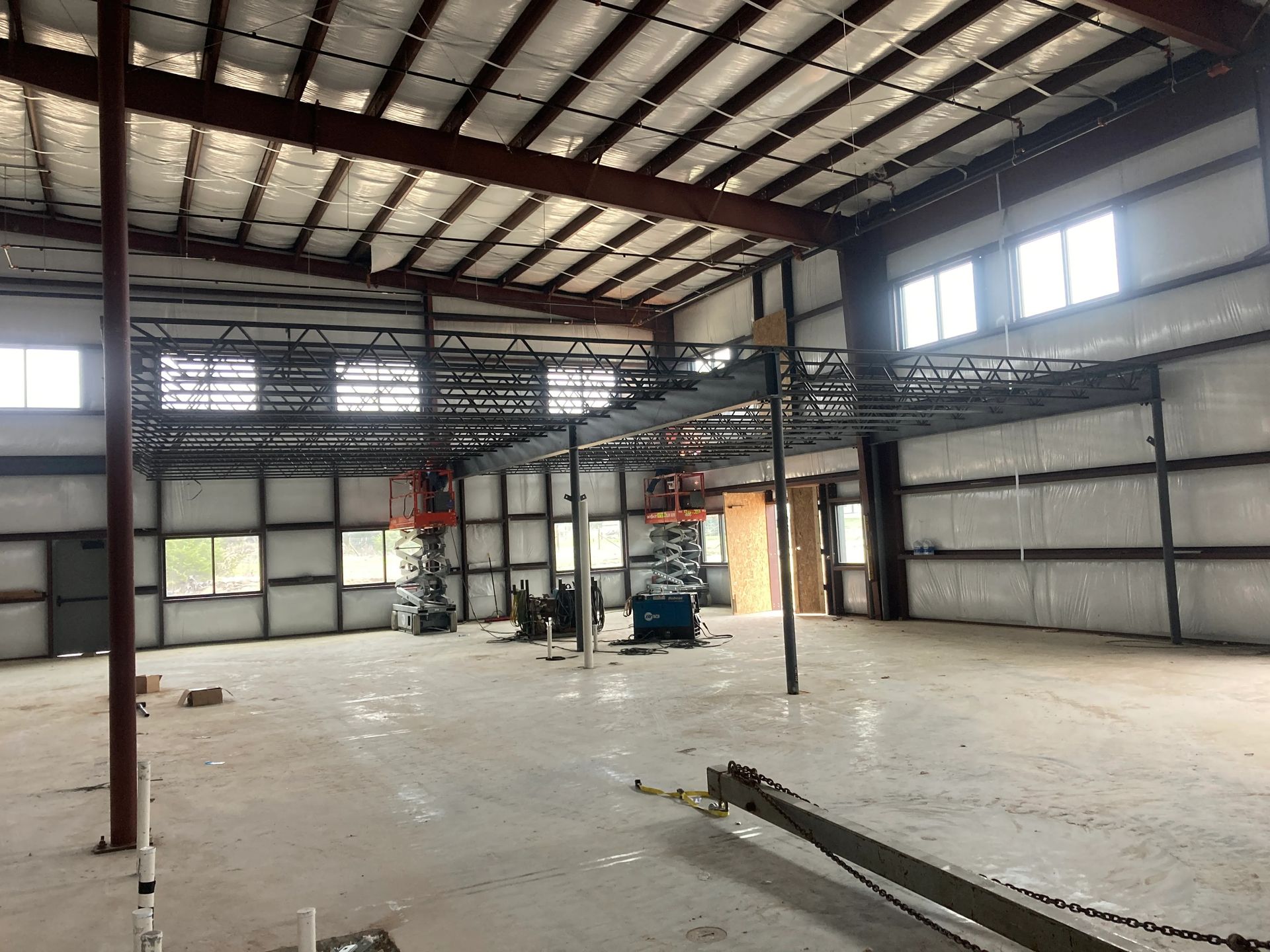 Empty industrial warehouse interior with metal beams, concrete floor, and a few scattered equipment pieces