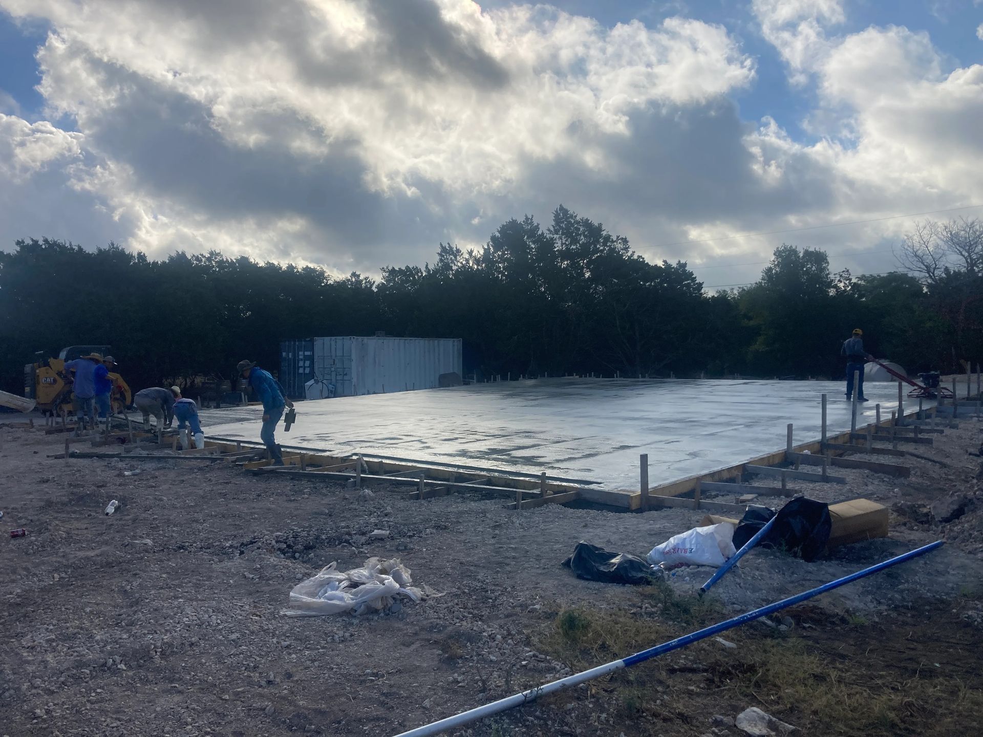 Outdoor construction site with a large concrete slab, workers, equipment, and cloudy sky