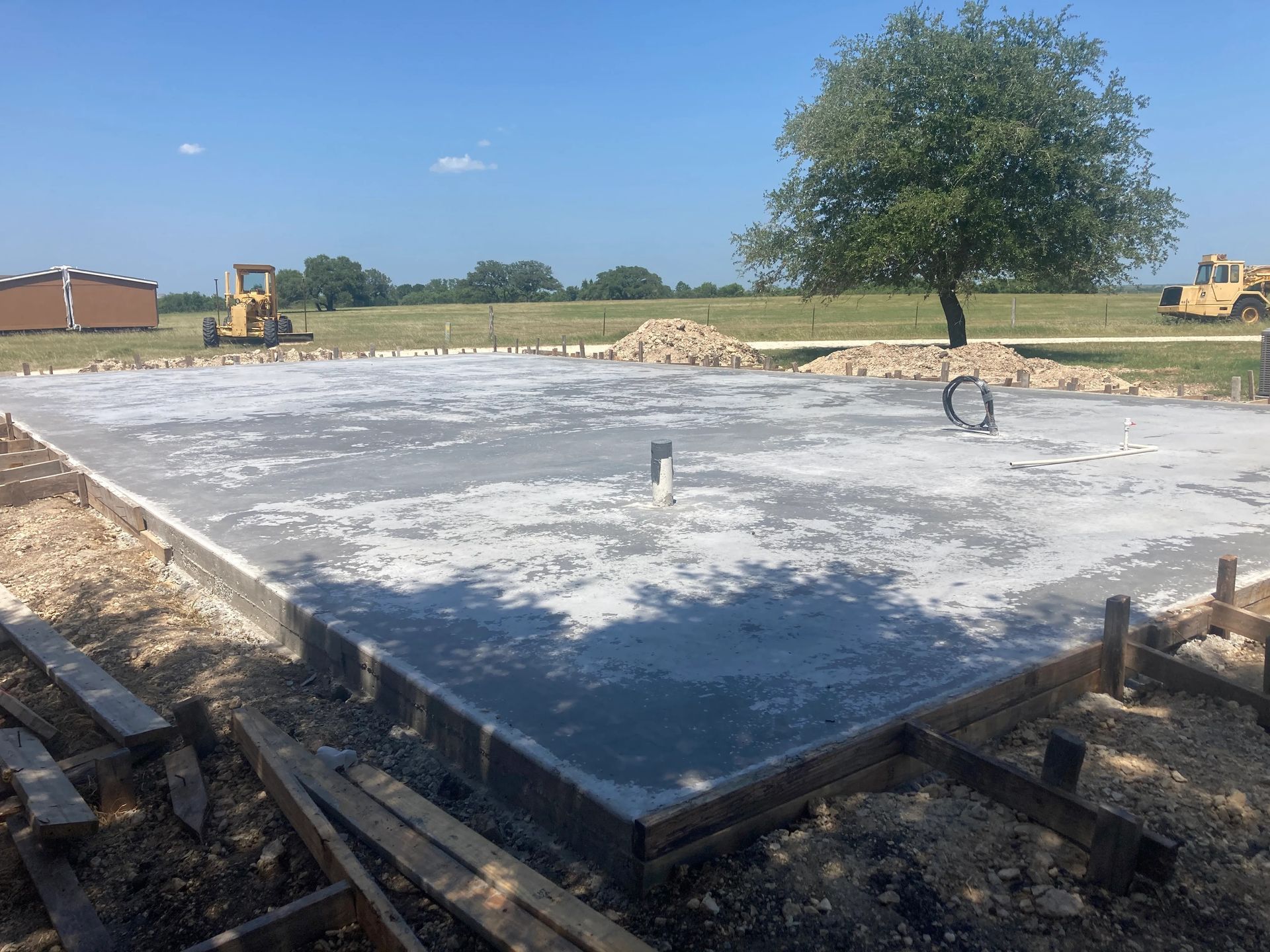 Concrete foundation slab being poured at a construction site on a sunny day.