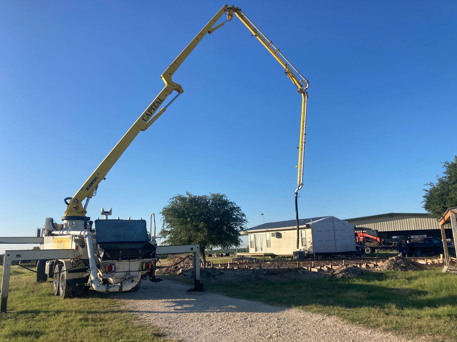 Concrete pump truck pouring from a long boom at a rural construction site under a blue sky