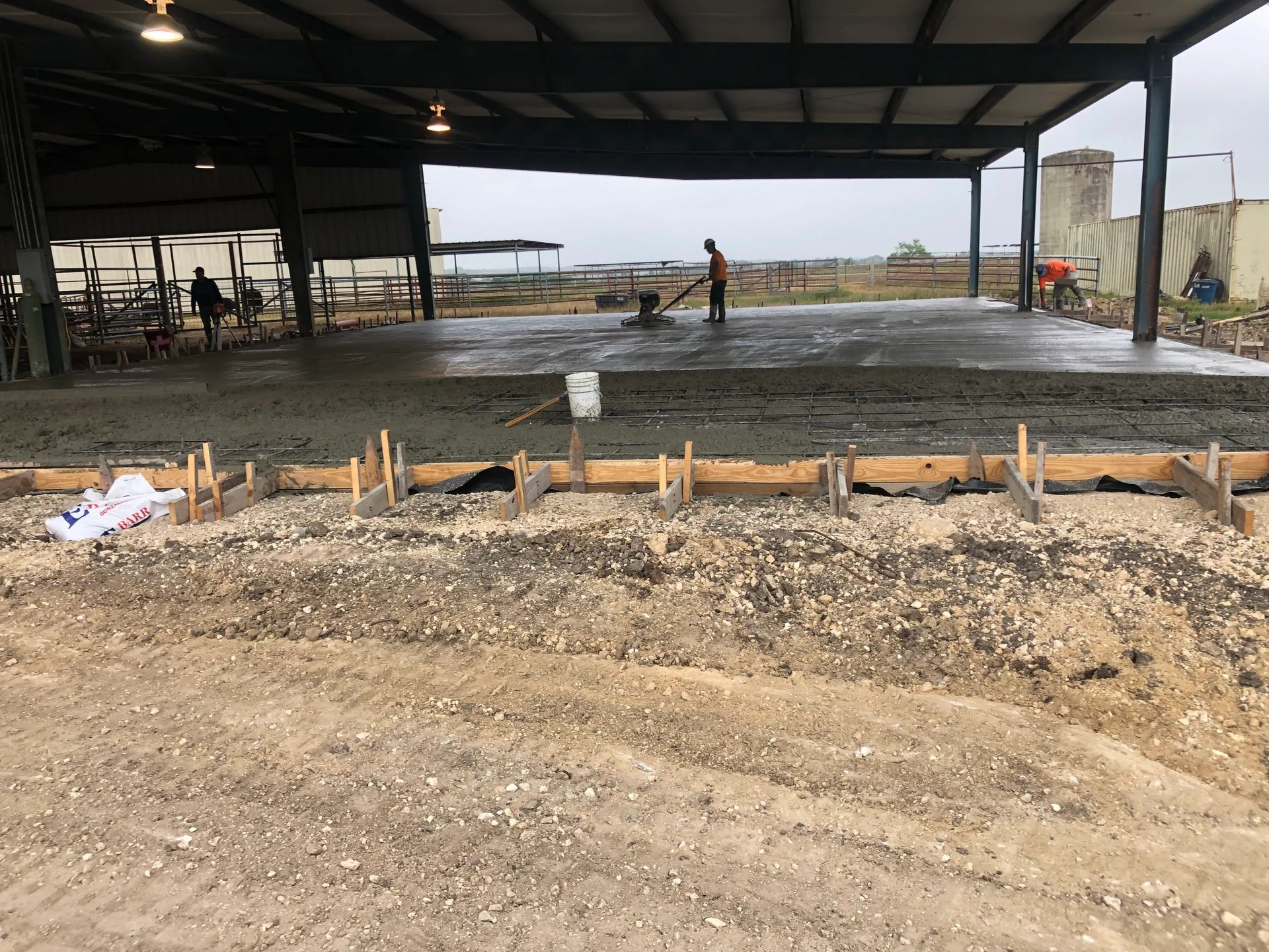 Concrete slab under construction in a large open-sided building with workers in the background.