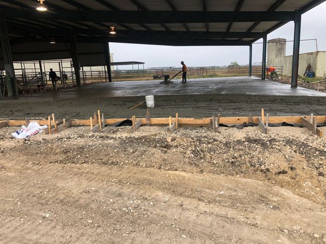 Concrete slab under construction in a large open-sided building with workers in the background.