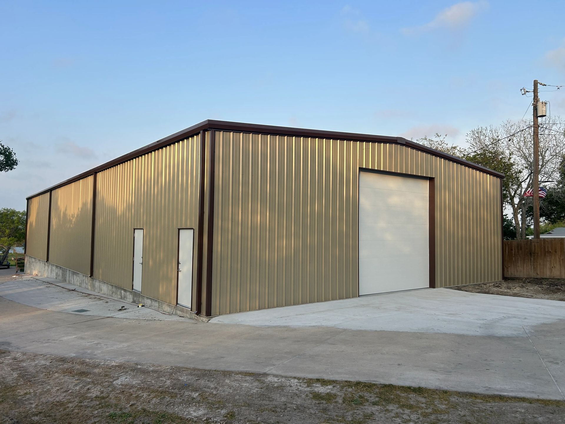 Tan metal warehouse with a large roll-up door on a concrete lot under a blue sky