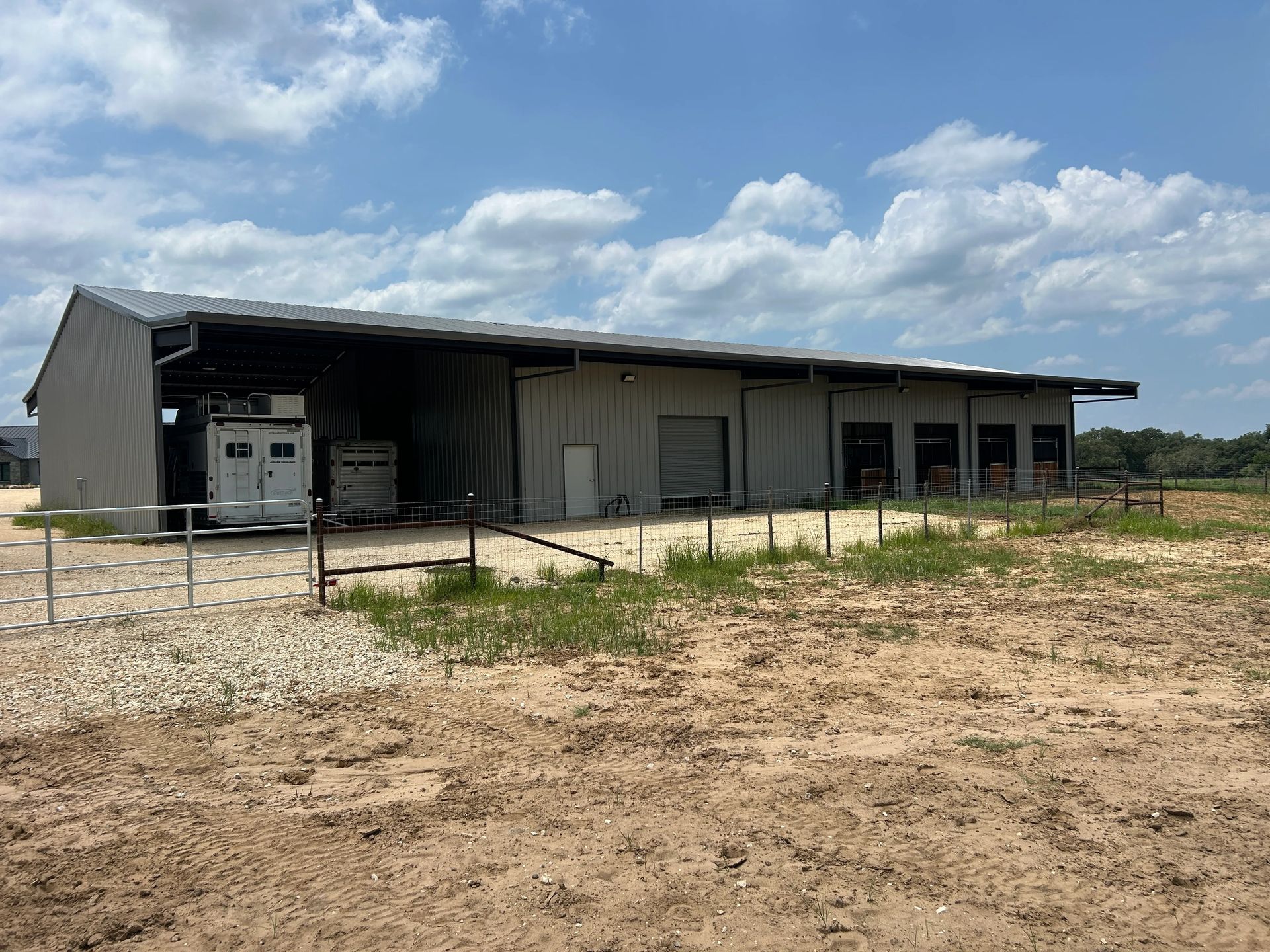 Long, low industrial warehouse with open bays in a dry, rural field under a cloudy sky