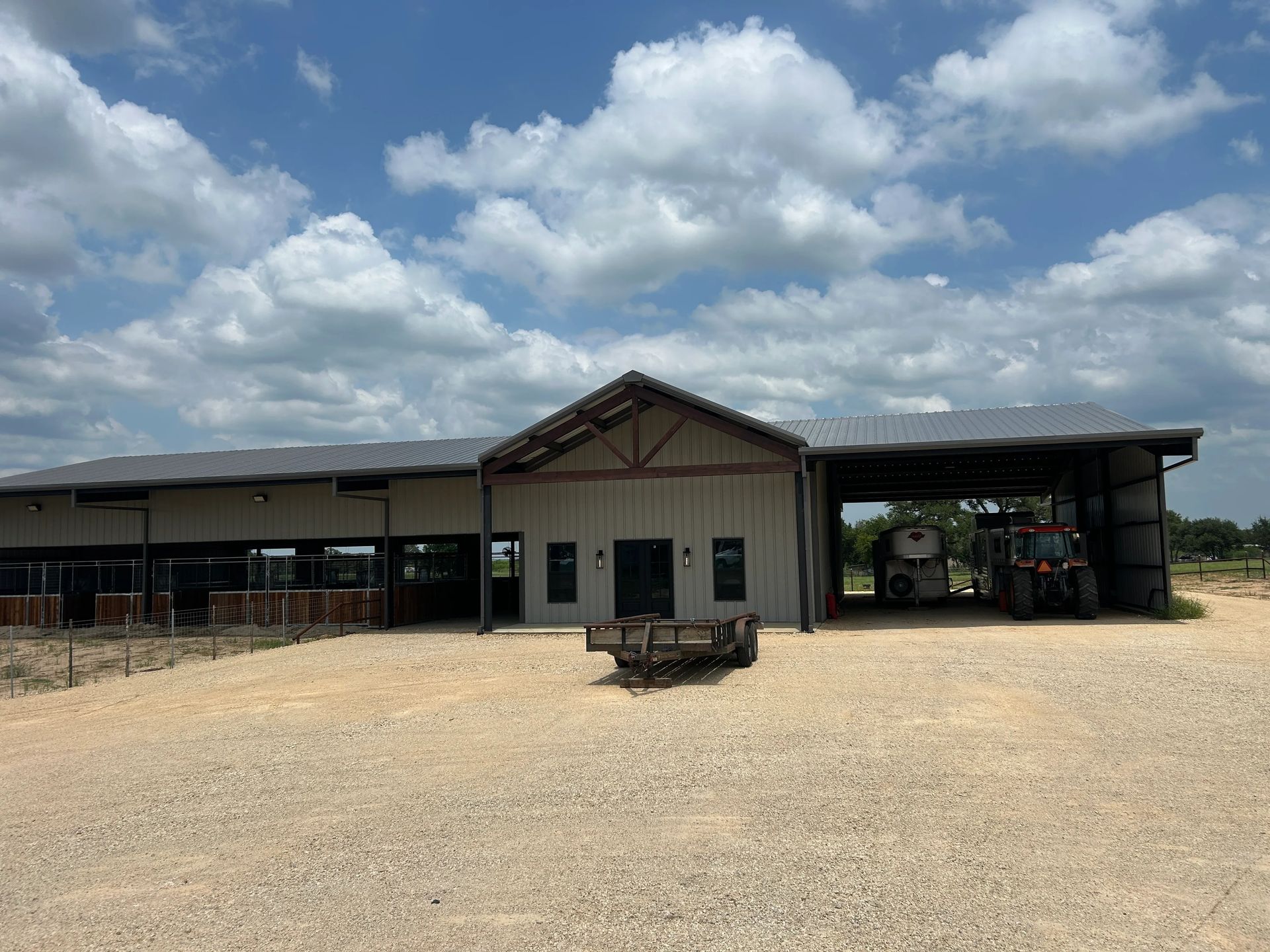 Rural building with a gabled roof and open-sided shed under a partly cloudy sky.