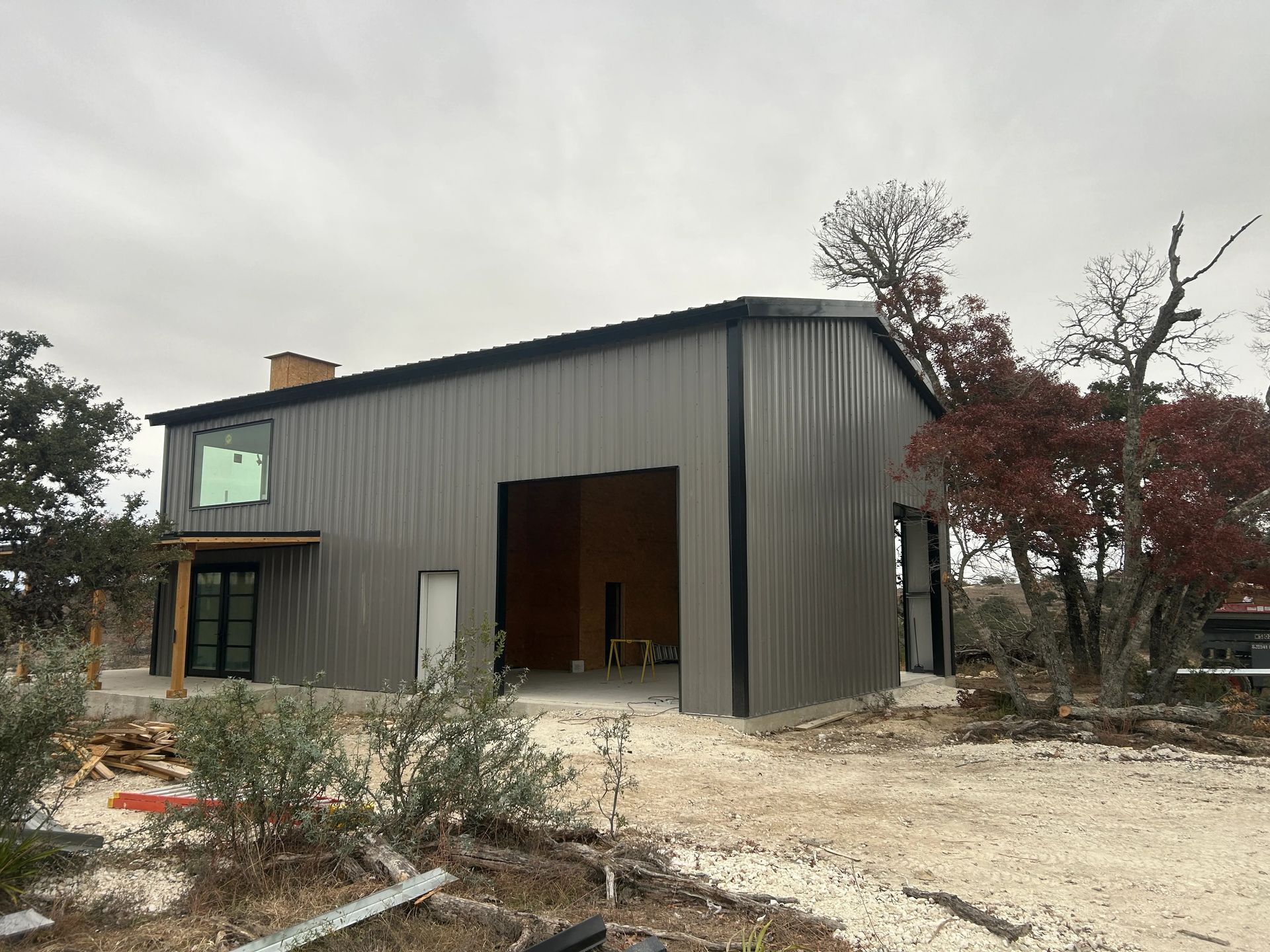Modern gray house exterior with large open doorway and bare landscaping under cloudy sky