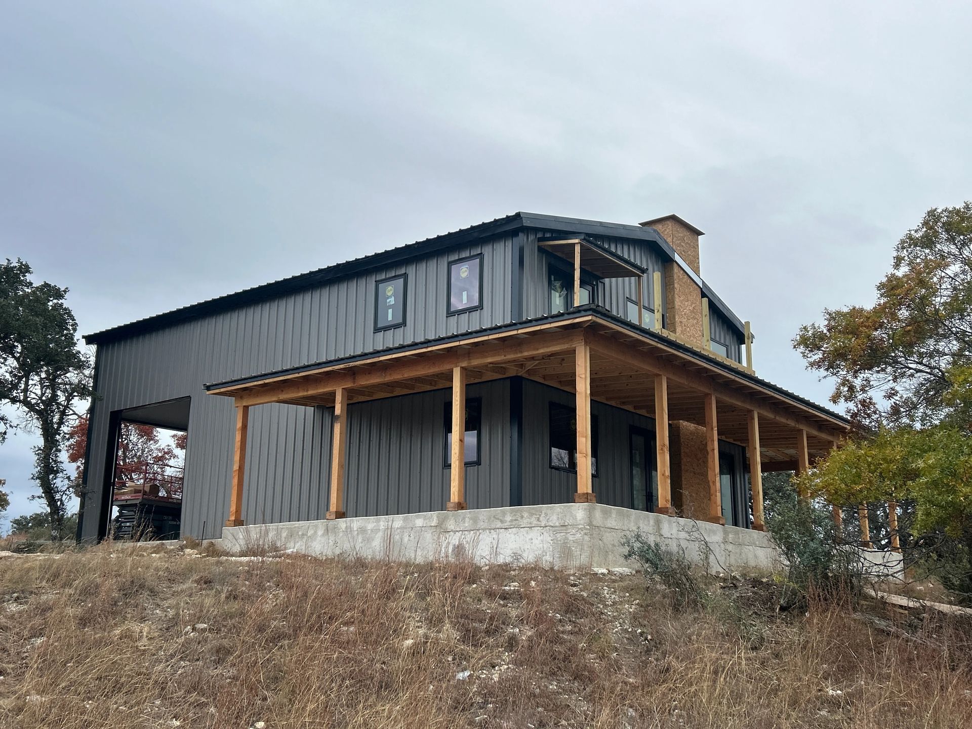 Modern black house with wood porch on a rocky hillside under an overcast sky