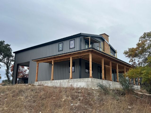 Modern black house with wood porch on a rocky hillside under an overcast sky