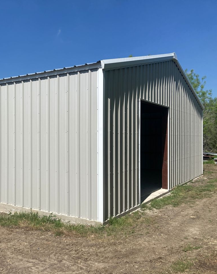 Gray metal shed with an open doorway on a dirt lot under a clear blue sky