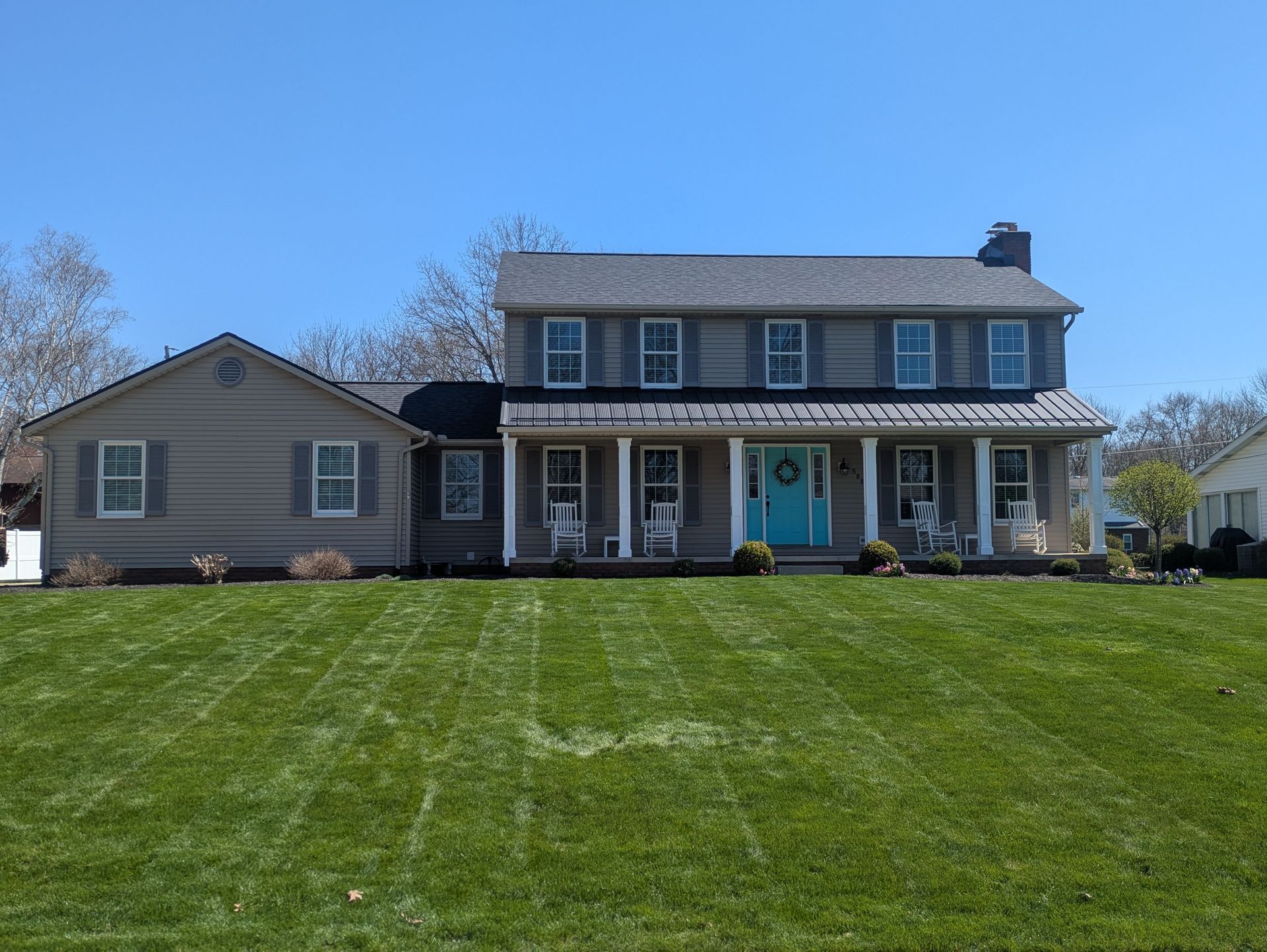 Suburban two-story house with blue shutters and a large green lawn under a clear sky