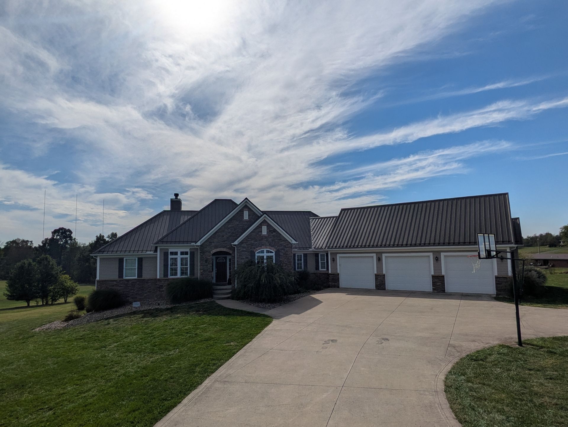 Suburban brick house with a large driveway and attached three-car garage under a cloudy sky