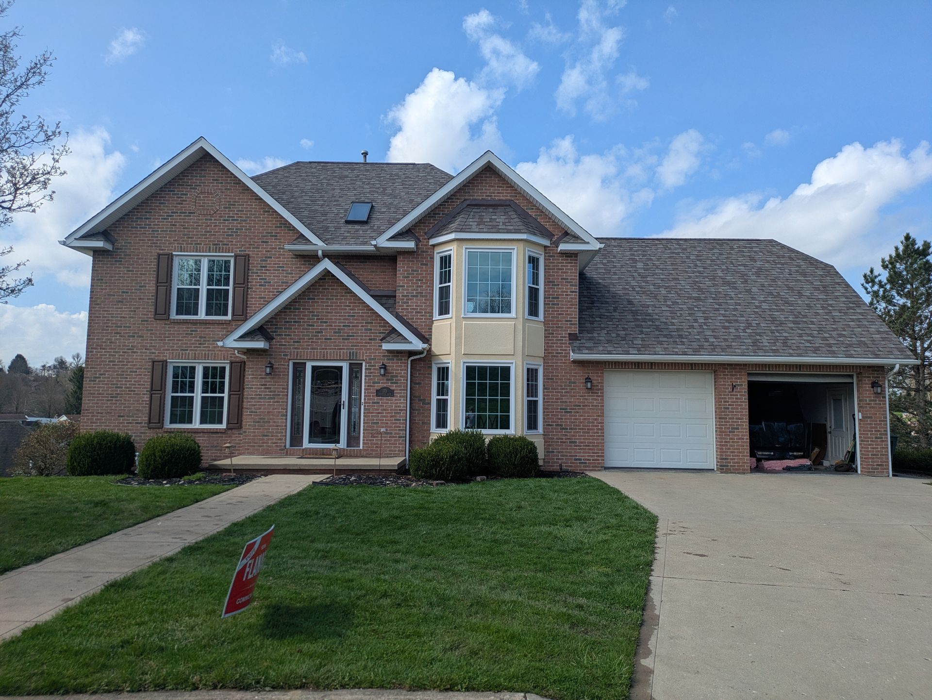 Two-story brick house with attached garage, front lawn, and driveway under a blue sky.