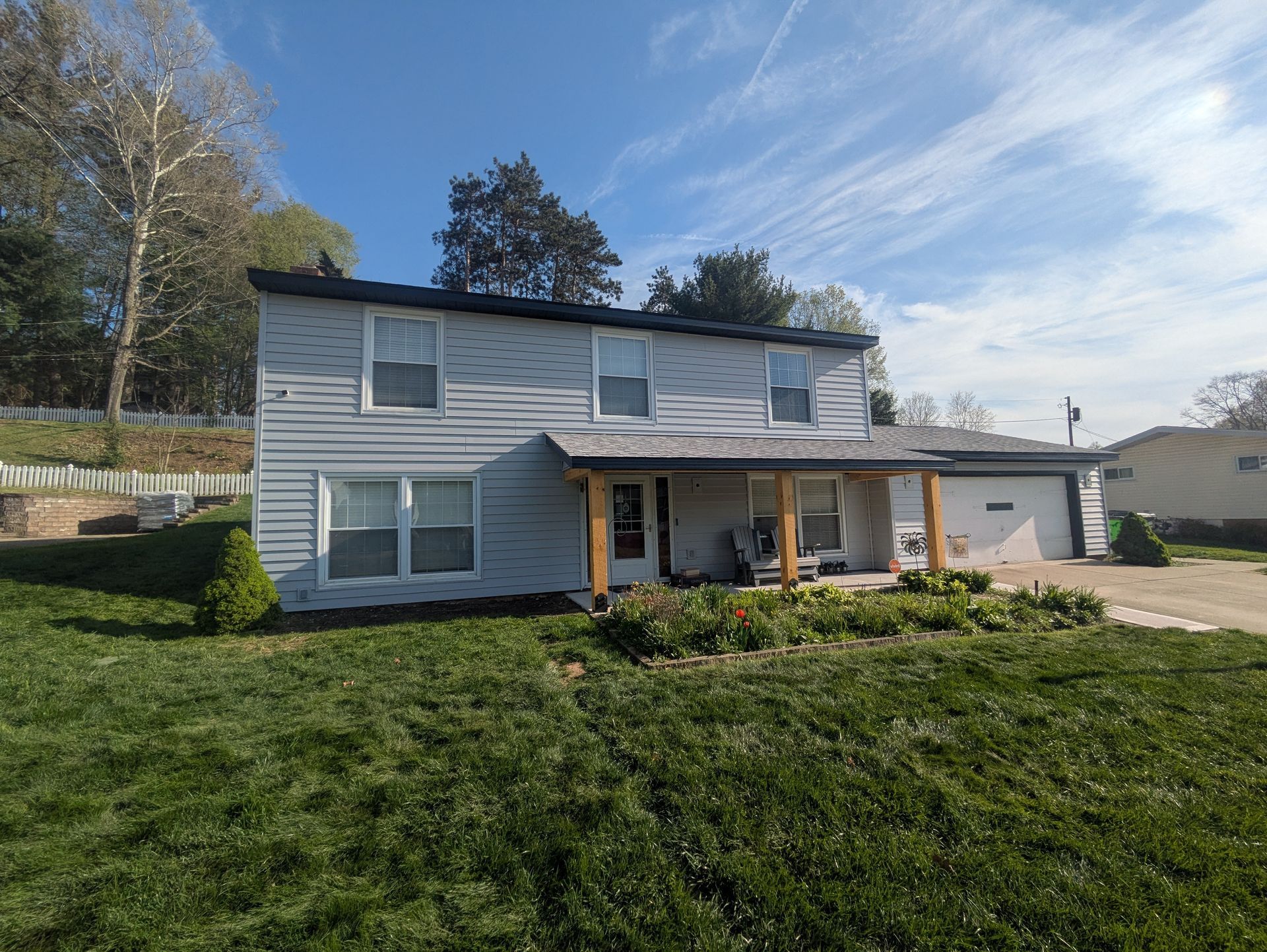 Two-story gray house with a covered porch and green lawn on a sunny day
