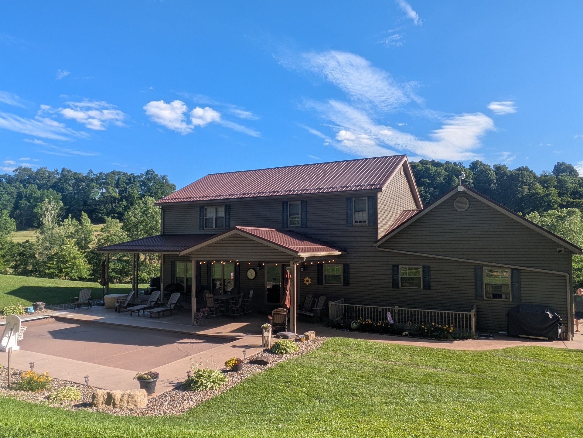 Rustic house with red roof and covered porch on a sunny green lawn under a blue sky