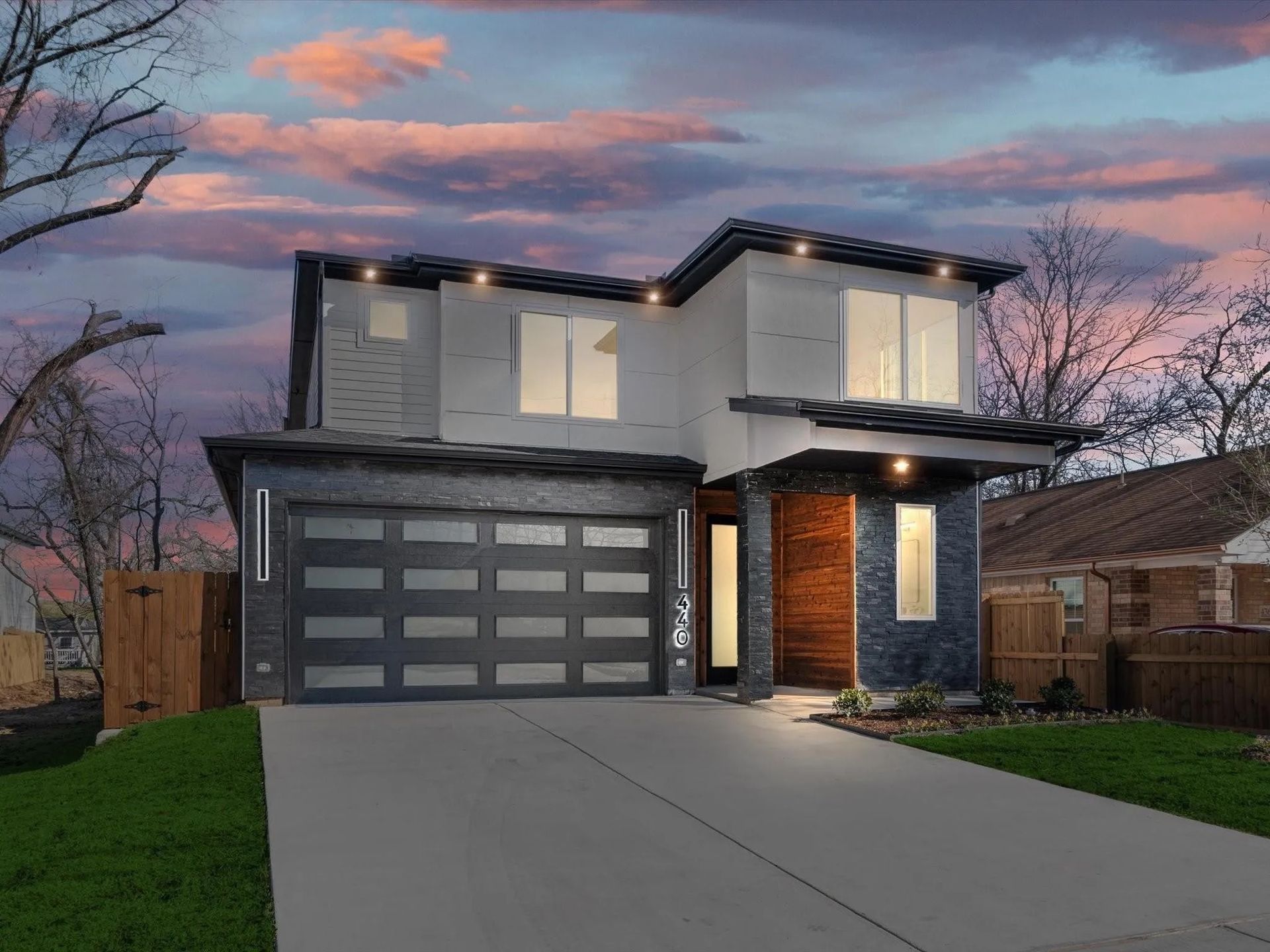 This modern home showcases a sleek design with a dark-toned garage, large windows, and stylish lighting.