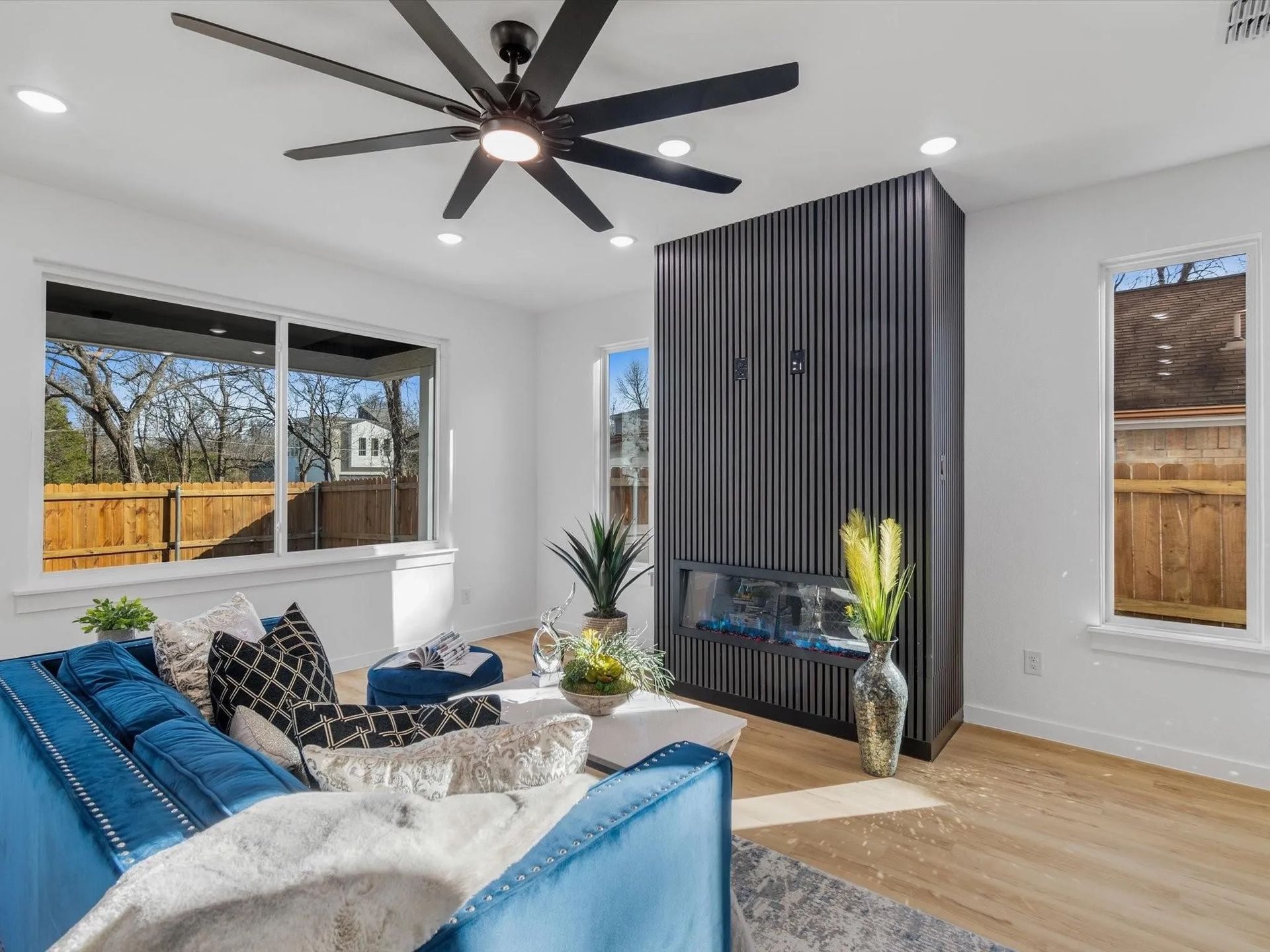 Bright living room with a blue couch, a black accent wall, and a large window overlooking a backyard. 