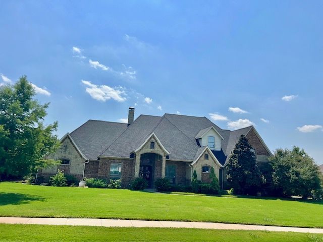 A large, two-story house with a dark roof and a manicured lawn under a blue sky.