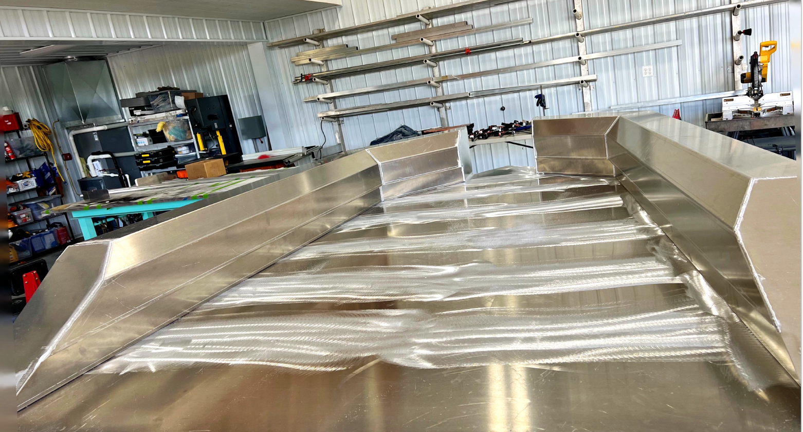 A stainless steel boat is sitting in the fabrication shop.