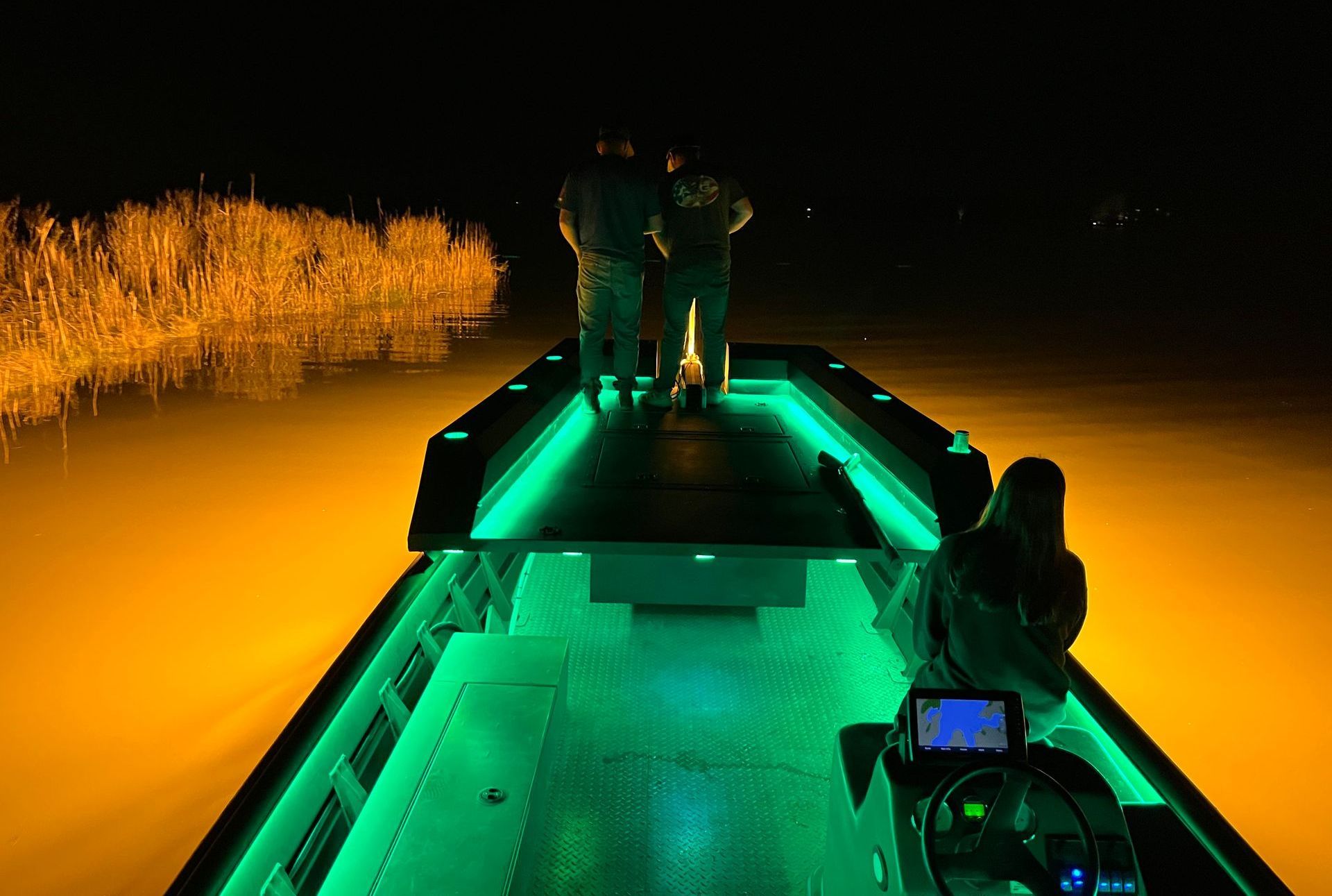 Two people are standing on the deck of a boat with green lights.