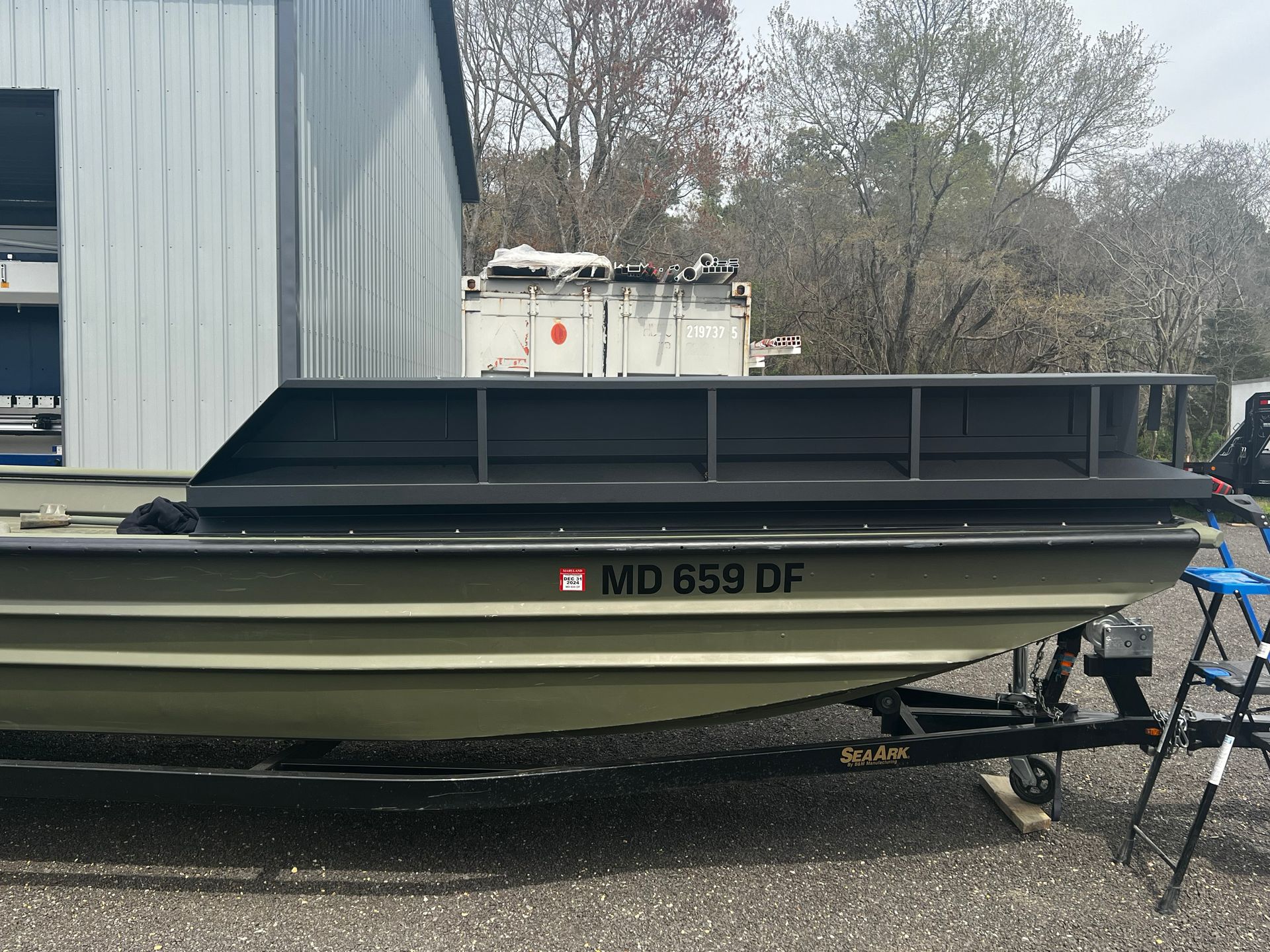 A hunting boat sitting on a trailer in front of the Invader Hunting Boat fabrication garage. 