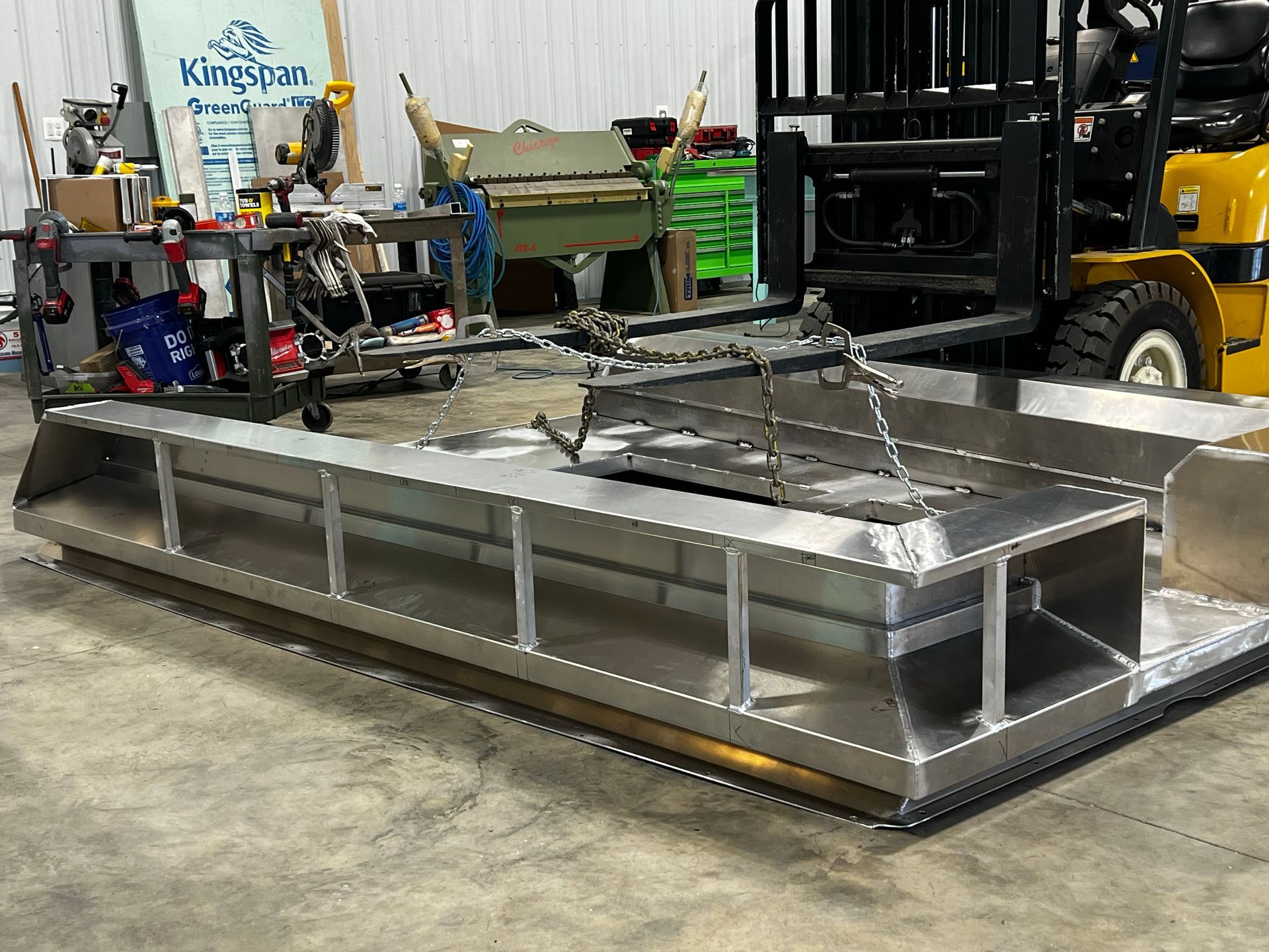 A forklift is sitting next to a large metal section of boat fabrication 