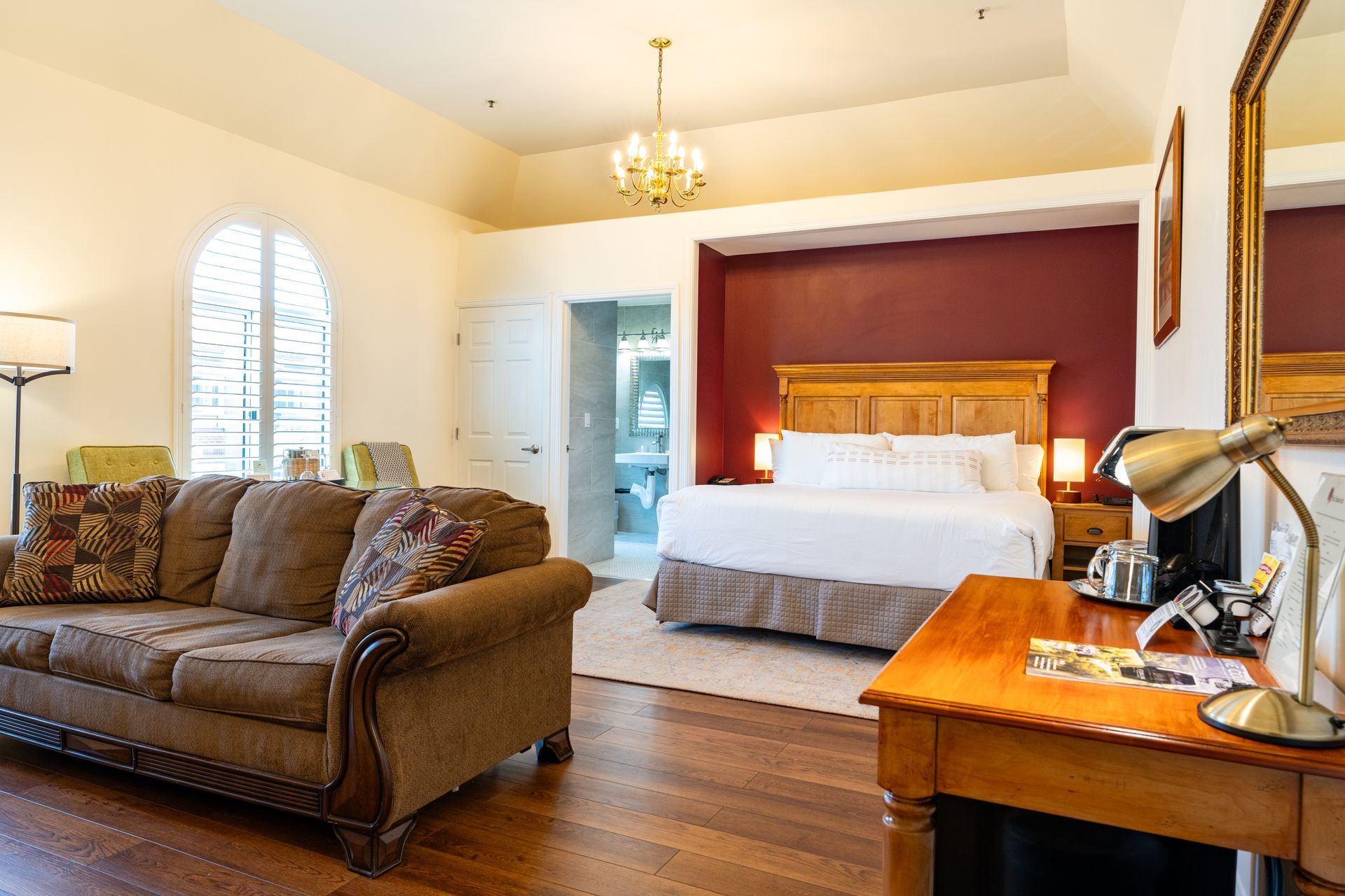 Spacious hotel room with a bed, sofa, desk, and arched window.