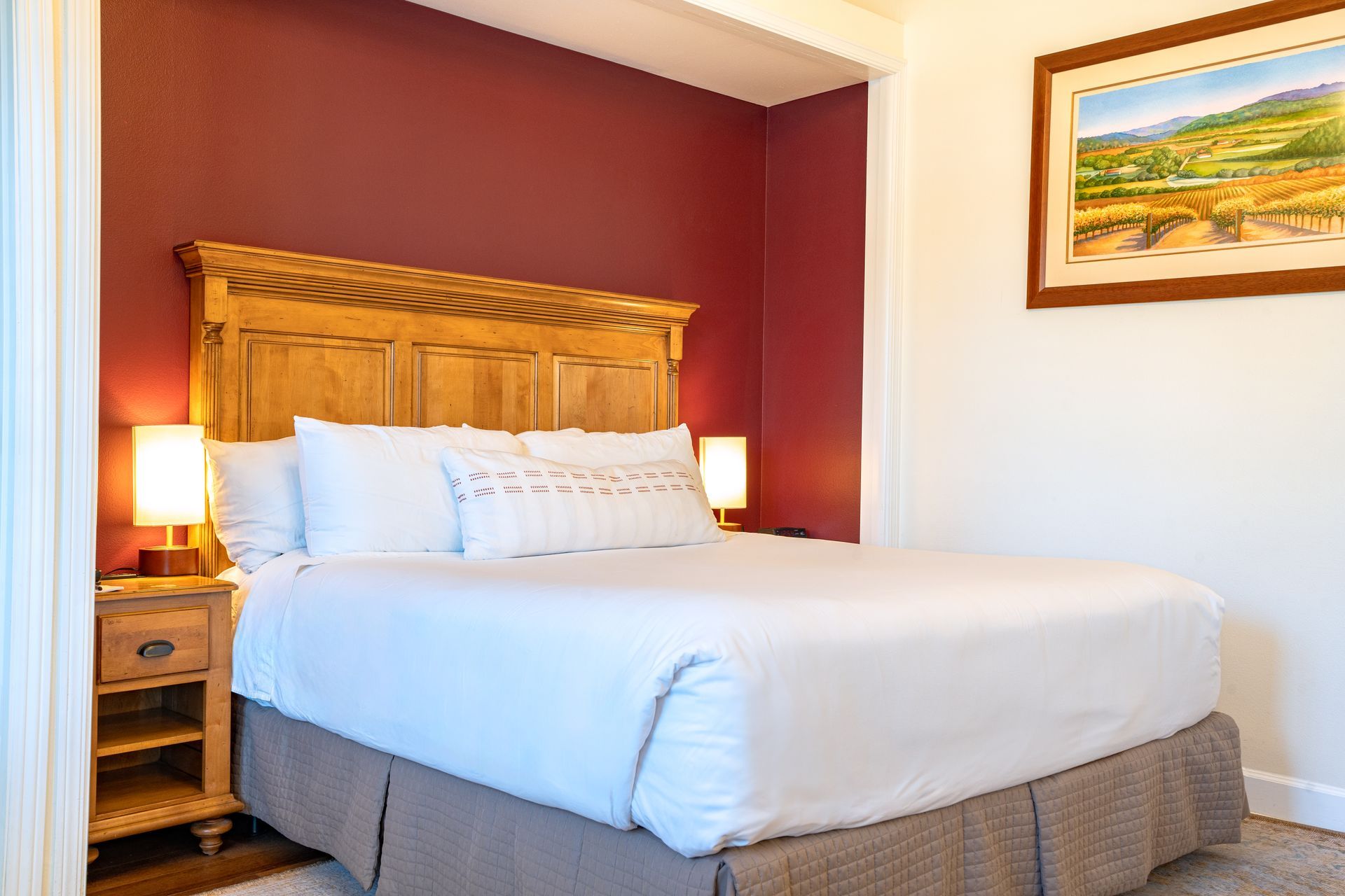 Bedroom with king bed, nightstands, and artwork on a burgundy accent wall.